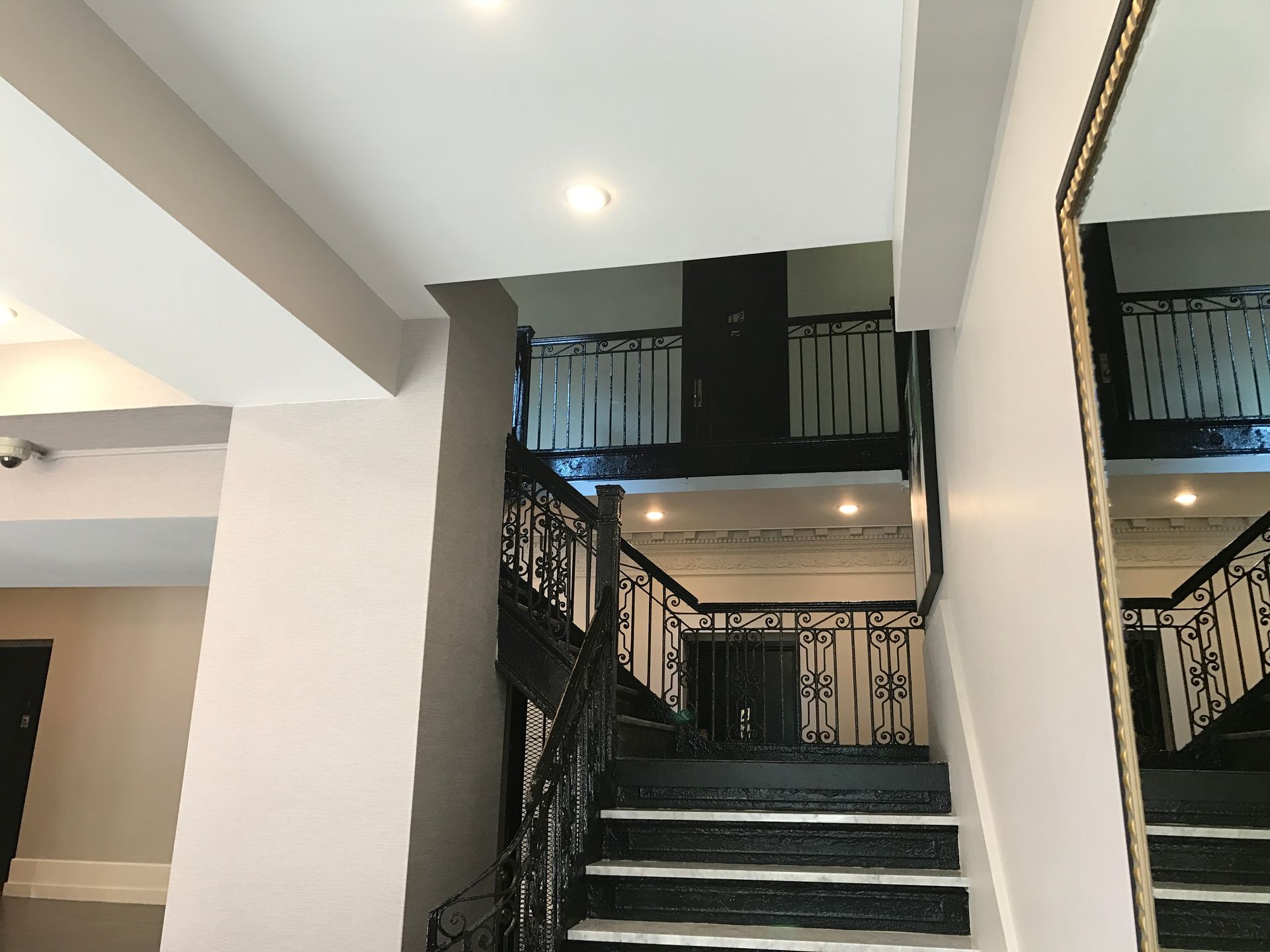 Indoor staircase with dark railings and recessed ceiling lights beside a large wall mirror