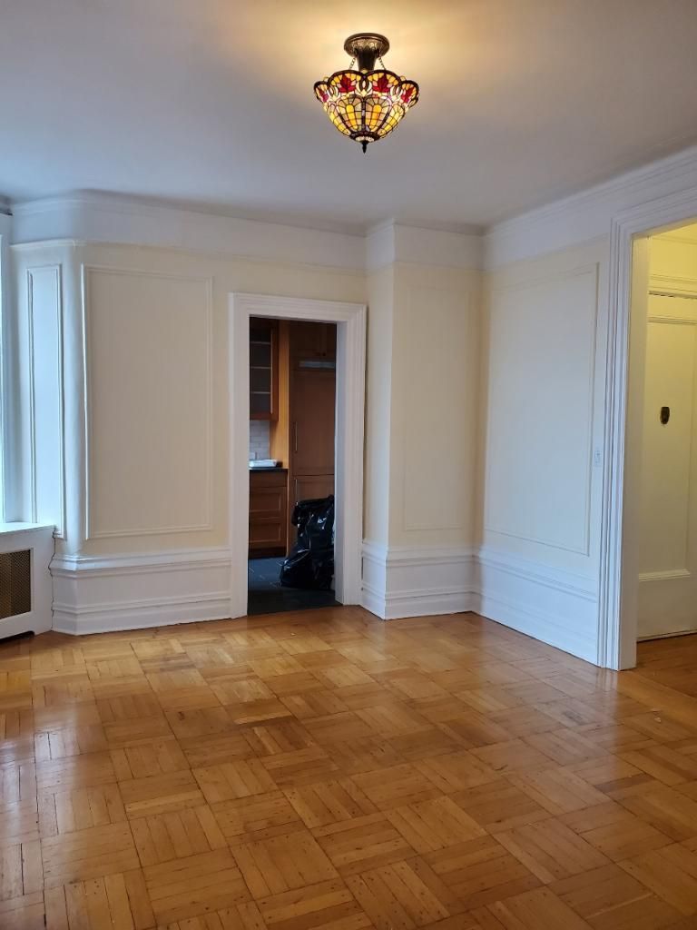 Empty room with hardwood floors, cream walls, white trim, and a small stained-glass ceiling light.