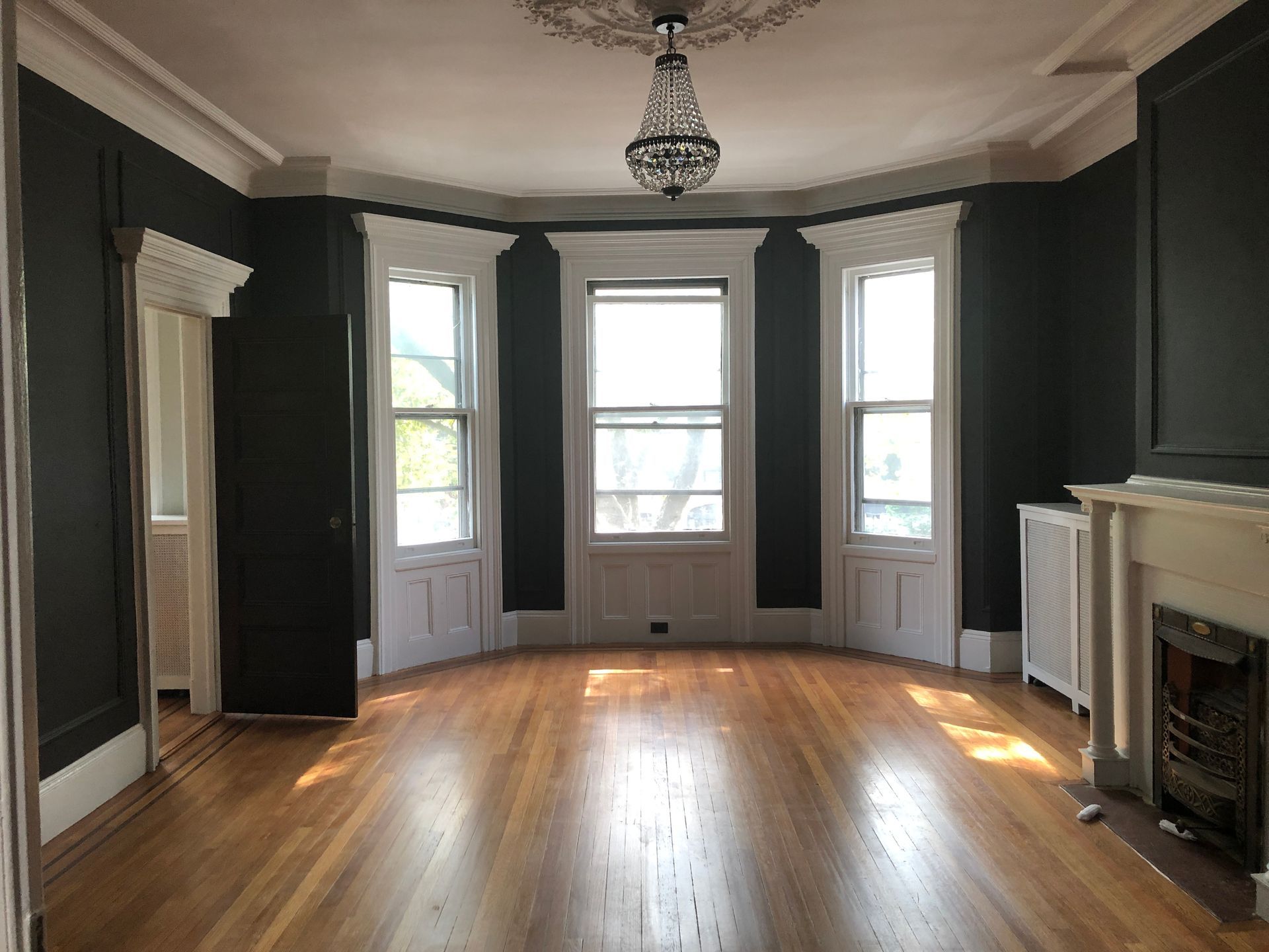 Empty living room with dark walls, hardwood floors, bay windows, and a fireplace