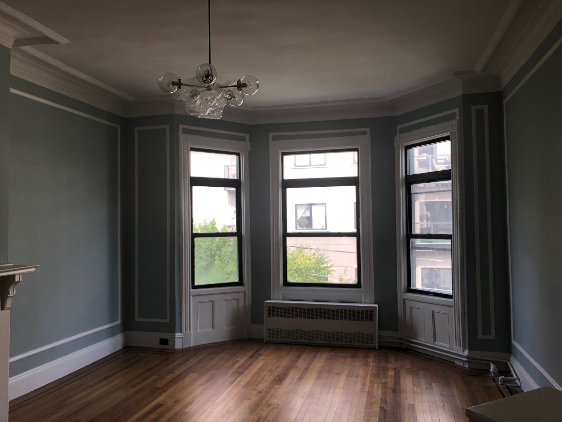 Empty room with gray walls, bay windows, hardwood floor, and a chandelier.