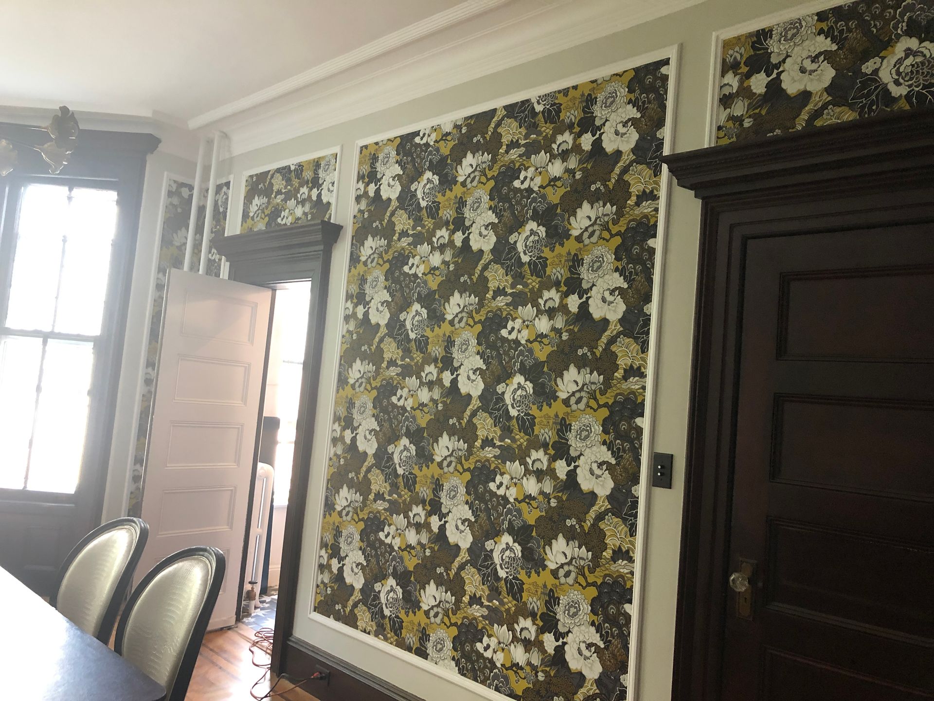 Elegant room with dark floral wallpaper, tall windows, and dark wood trim and door.