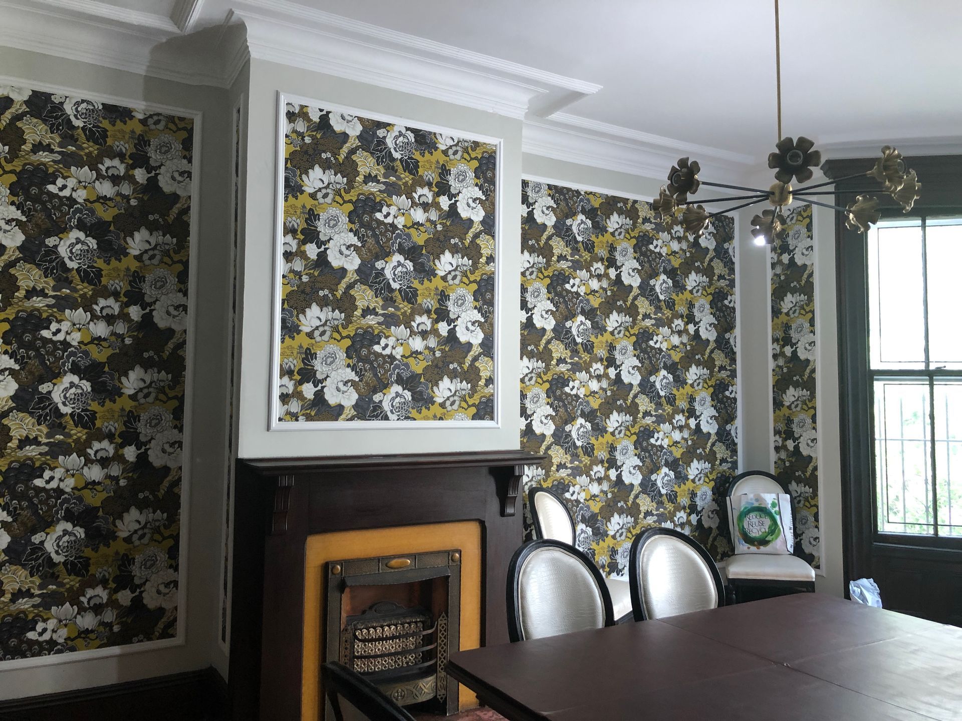 Dining room with floral wallpaper, fireplace, white trim, and silver chairs near a window