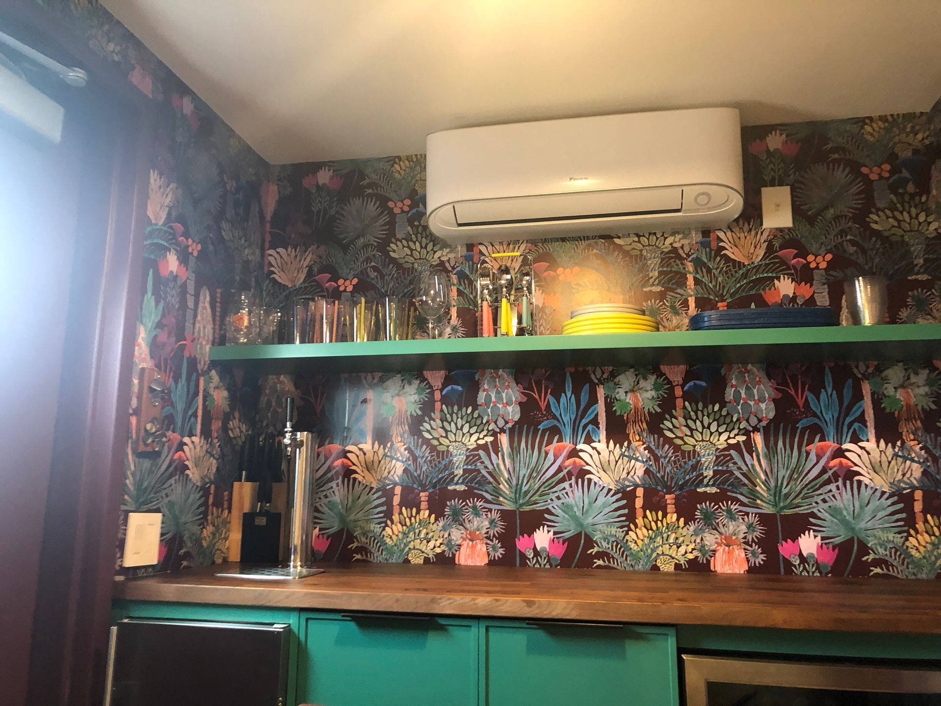 Colorful tropical-themed room with floral wallpaper, green shelves, and a wall-mounted air conditioner.