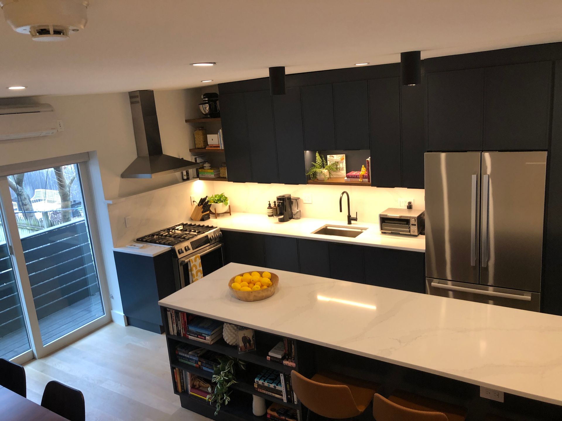 Modern kitchen with dark cabinets, white island countertop, stainless fridge, and fruit bowl.