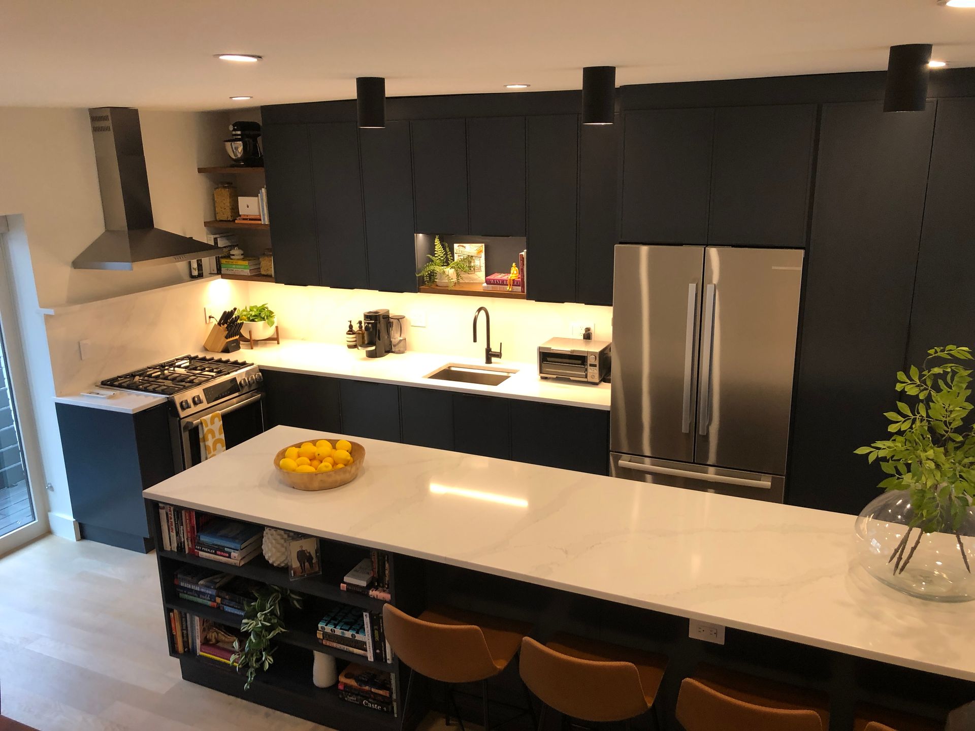 Modern kitchen with black cabinets, white island, stainless fridge, and fruit bowl on the counter