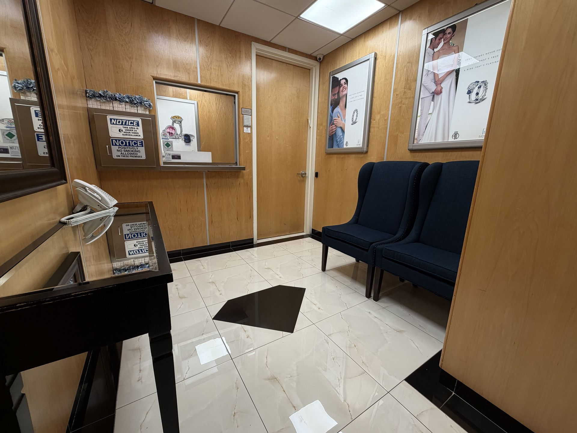 Empty waiting room with blue chairs, wood-paneled walls, posters, and white tile flooring.