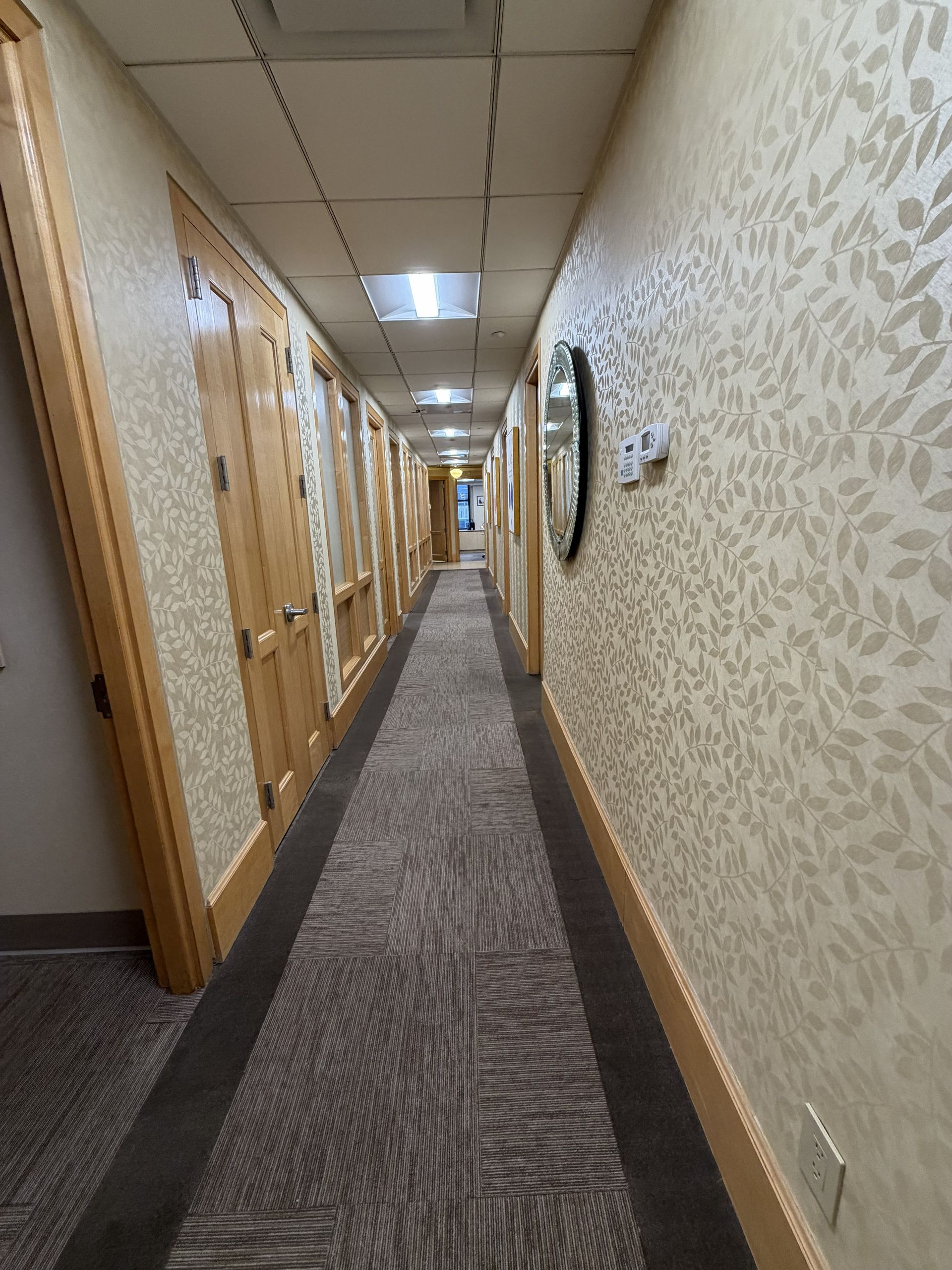 Narrow hotel hallway with patterned carpet, beige walls, wooden doors, and ceiling lights