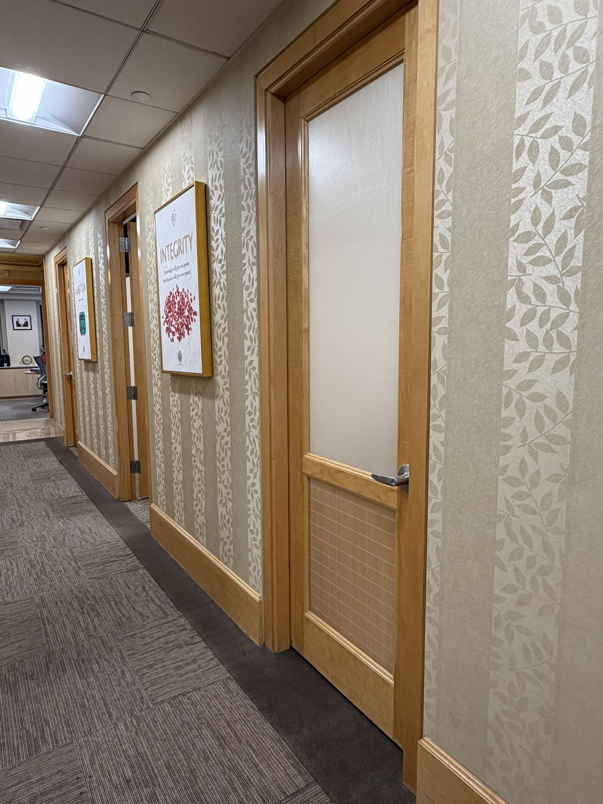 Office hallway with beige patterned wallpaper, wood doors, and carpeted floor