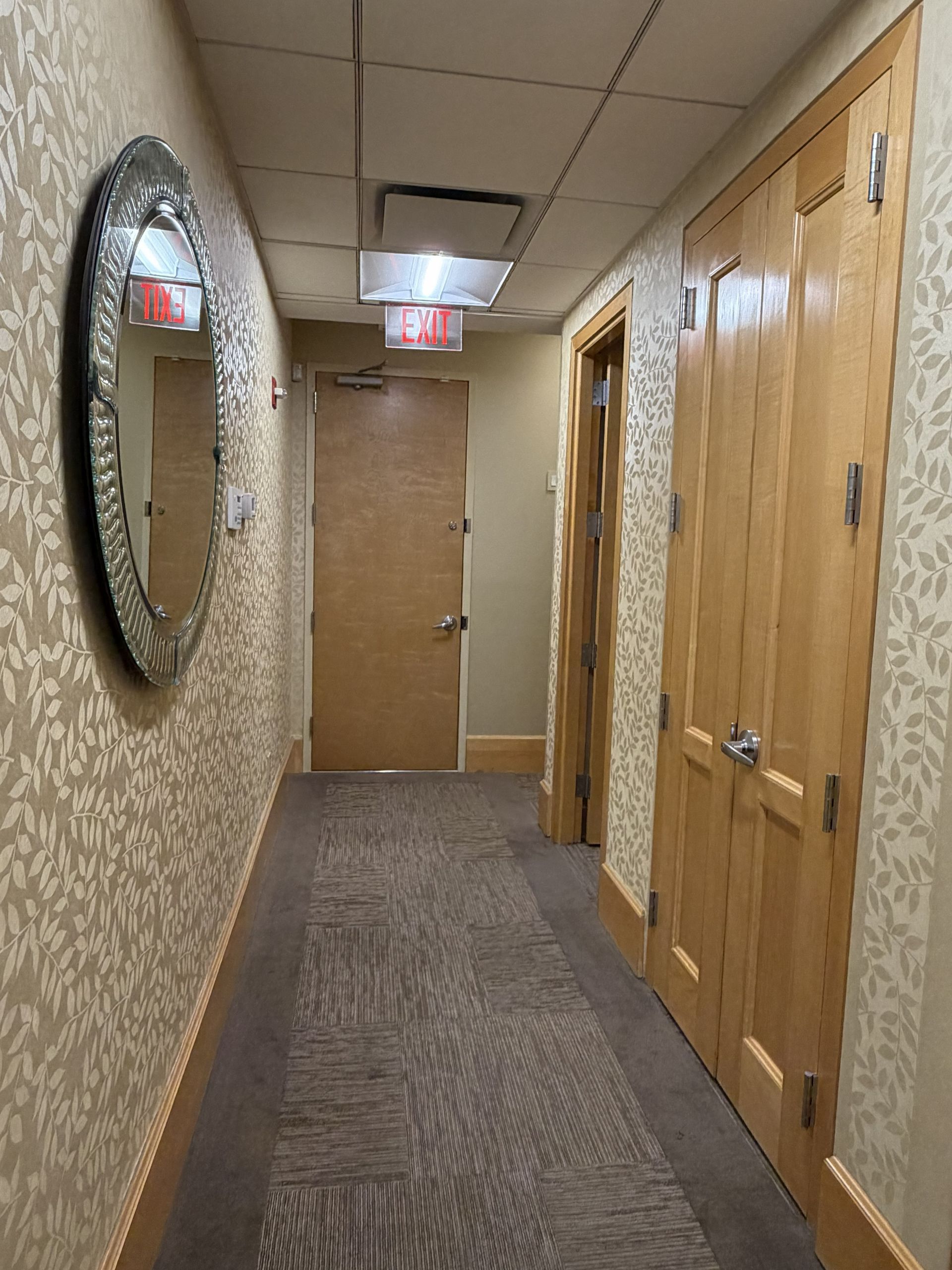 Long beige hallway with patterned wallpaper, carpet, wood doors, and ceiling lights