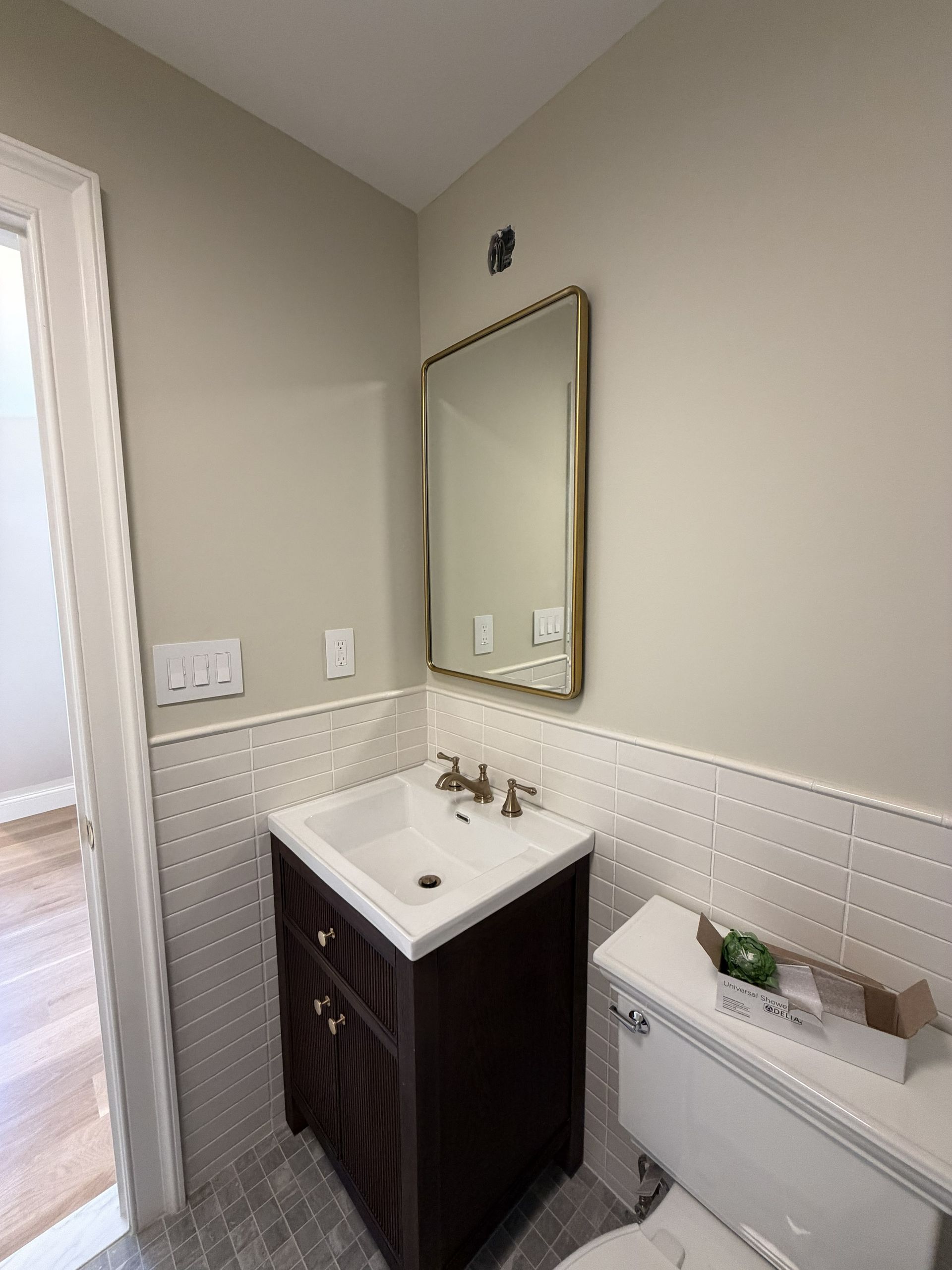 Small bathroom sink with dark vanity, mirror, and white toilet against light gray walls and tile.