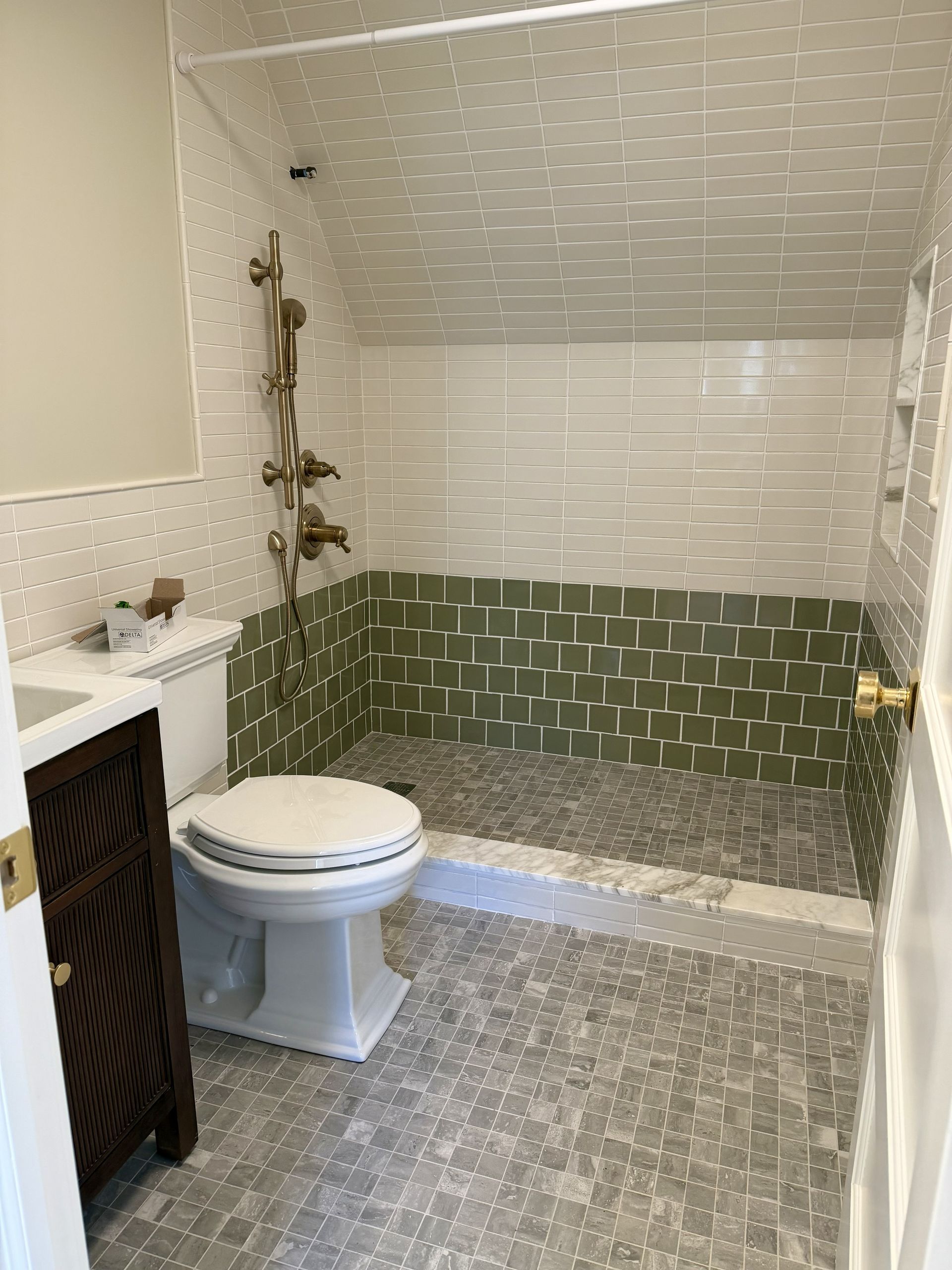 Small bathroom with white toilet, dark vanity, and shower tiled in green and white.