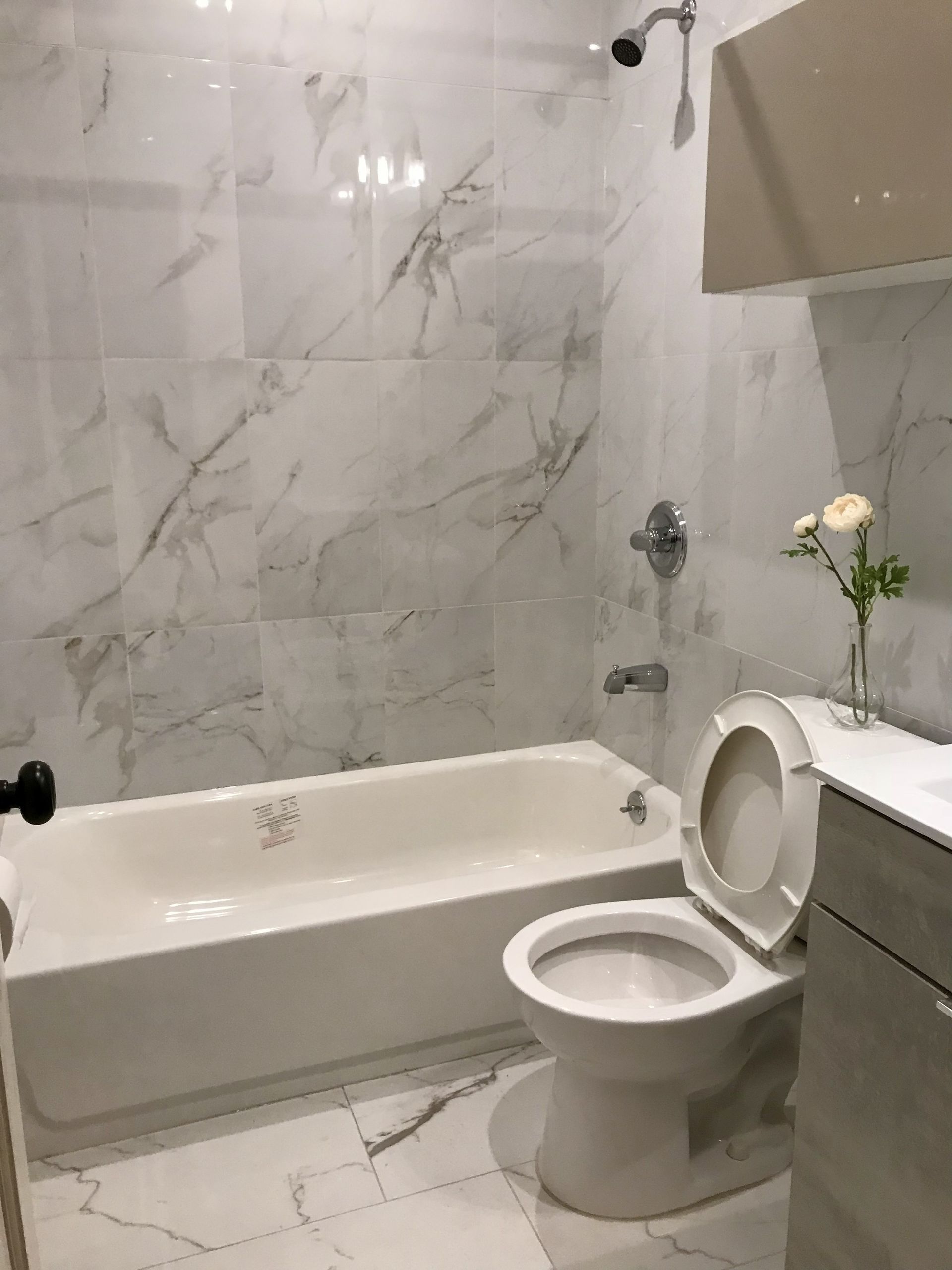 Bathroom with marble tile, bathtub, toilet, and a sink cabinet; a vase with flowers sits on the counter.