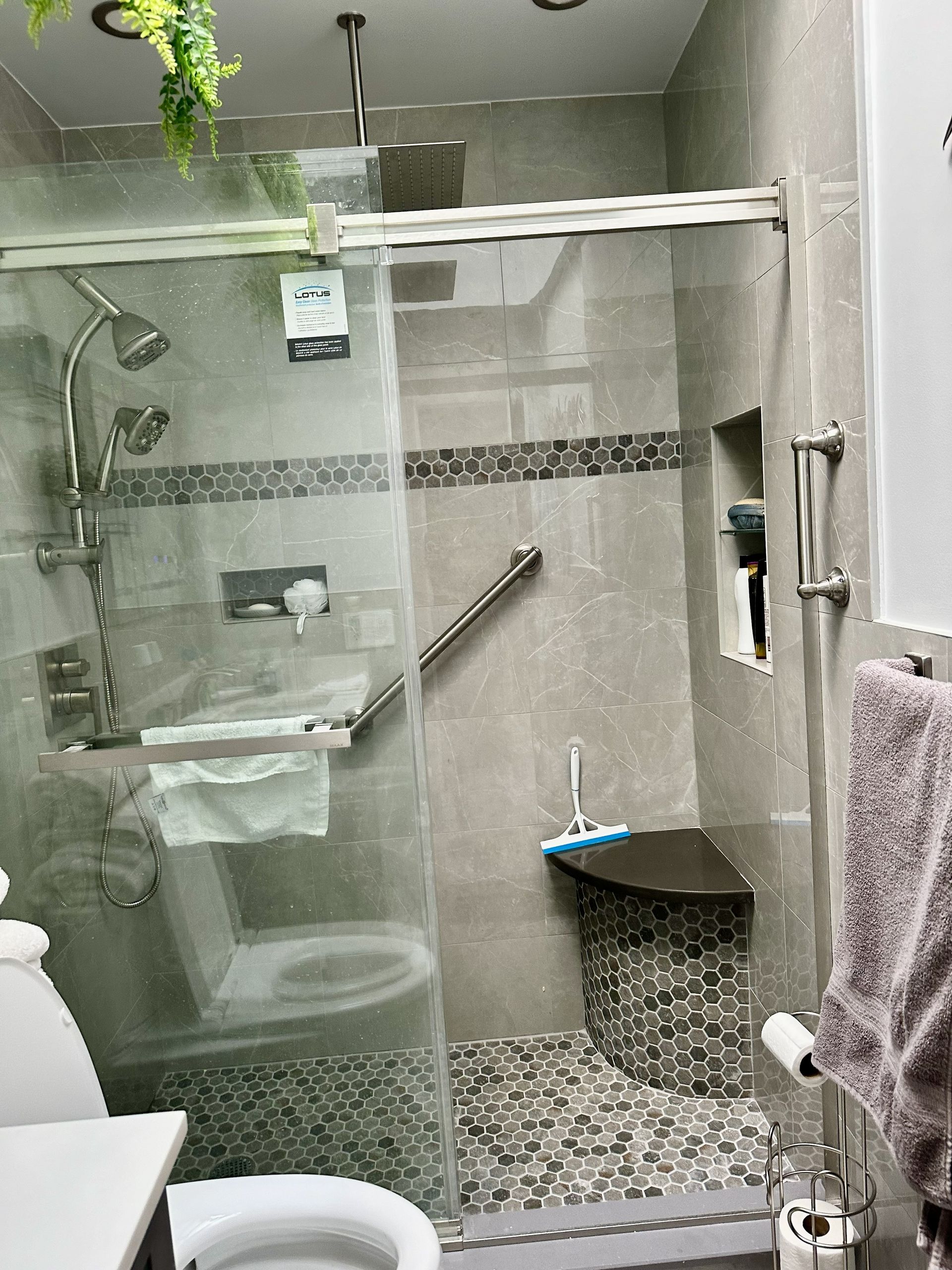Small bathroom with a glass shower, pebble tile floor, wall shelf, and towel rack.