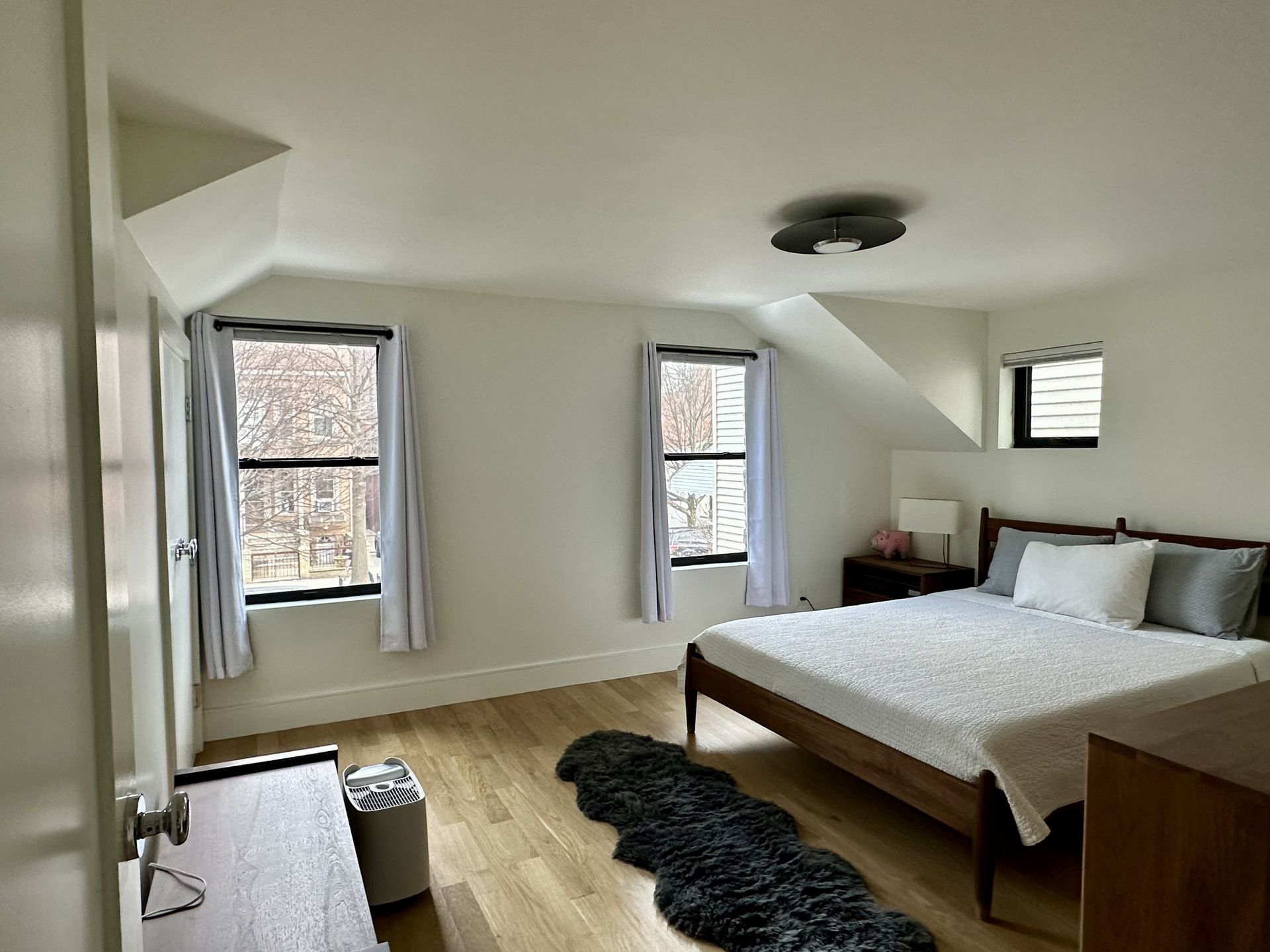 Bright bedroom with a bed, windows, light wood floor, and a black shag rug