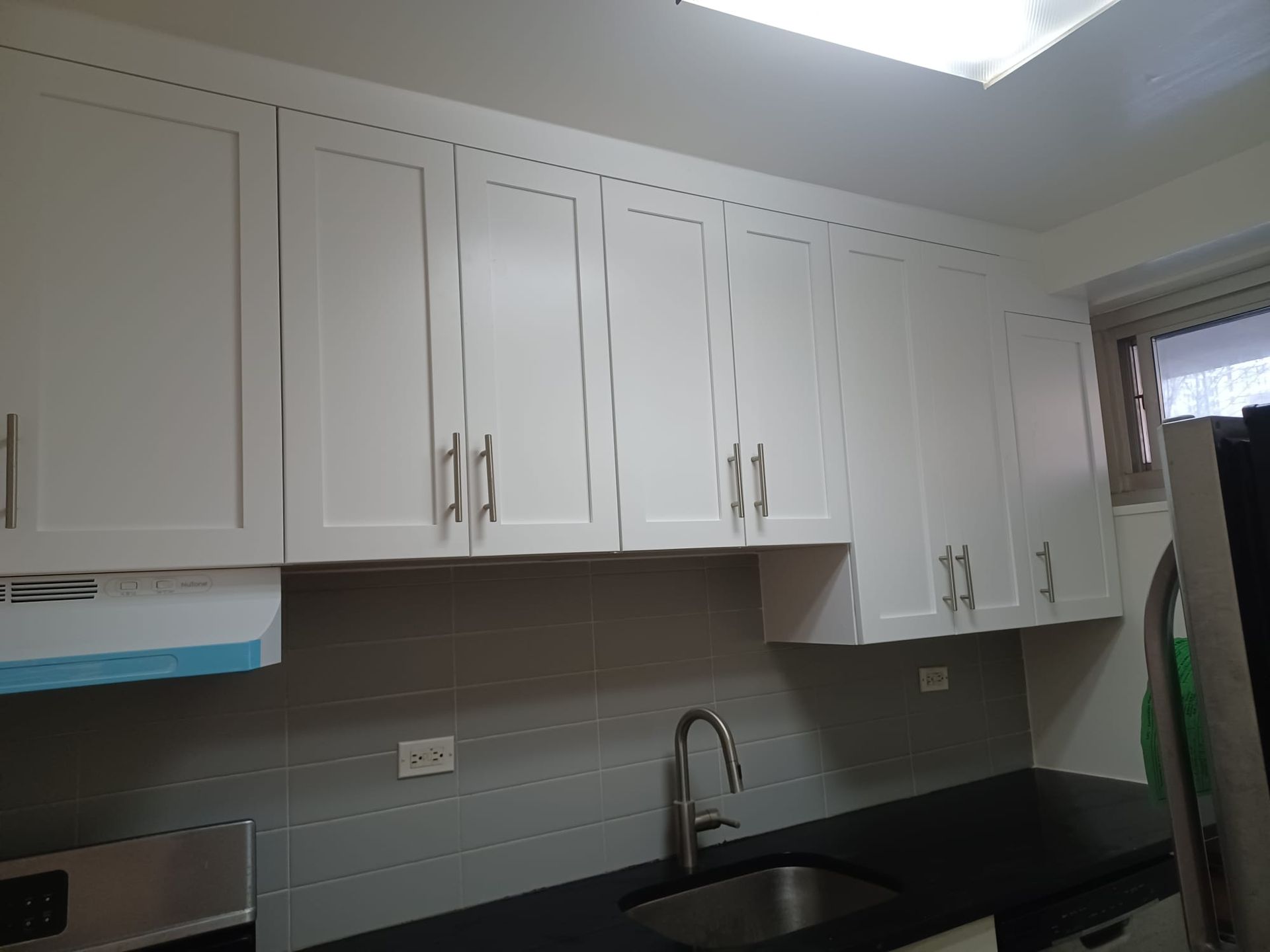 White kitchen cabinets above a black countertop and sink, with a window on the right.
