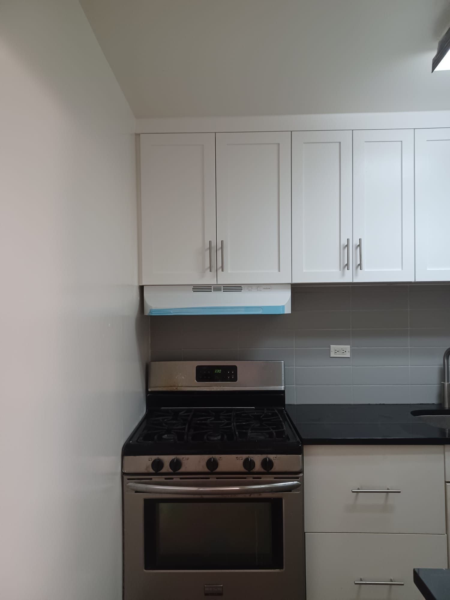 Compact kitchen with white cabinets, stainless steel stove, gray backsplash, and dark countertop.