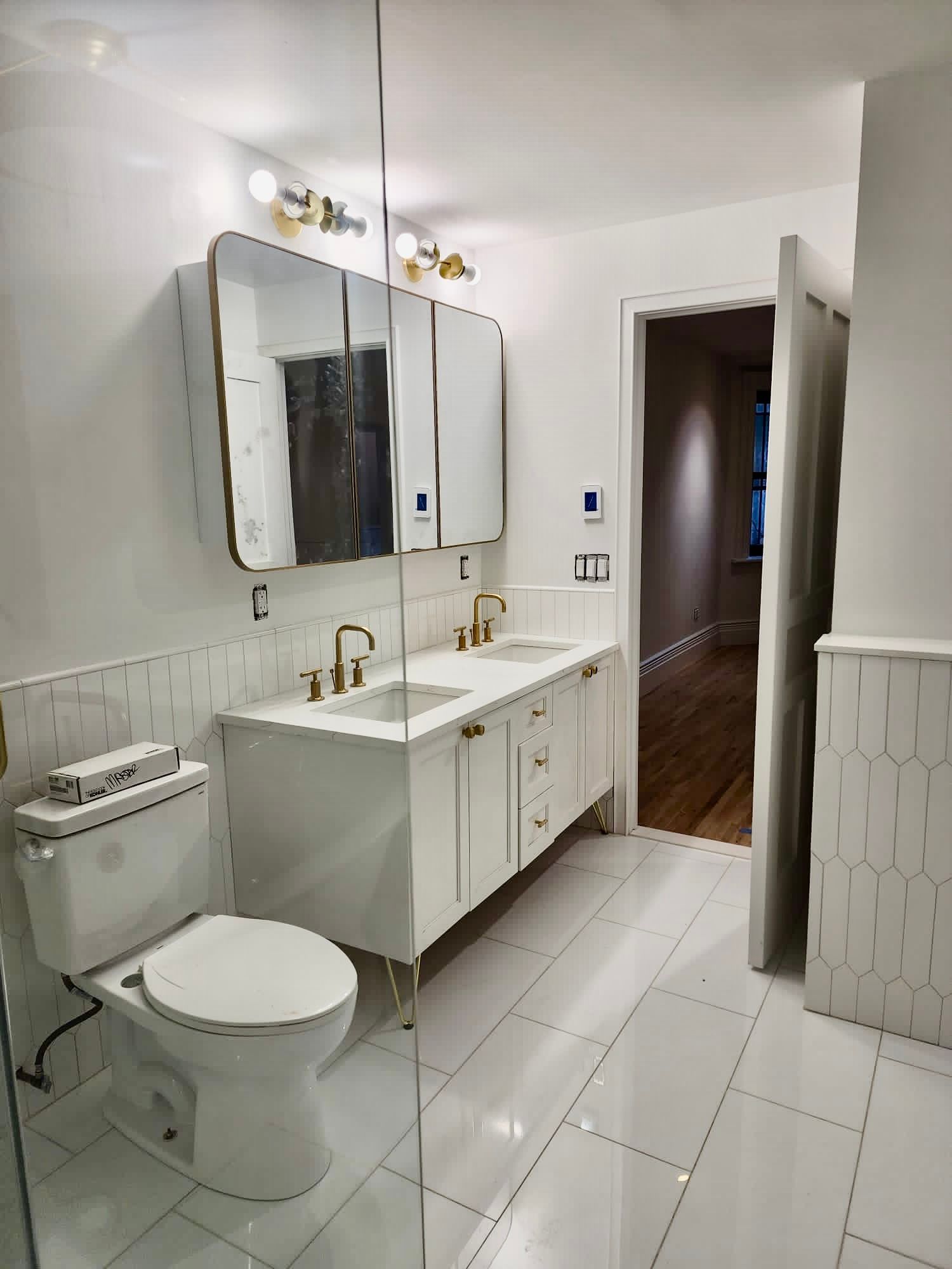 Bright white bathroom with vanity, mirror cabinet, toilet, sink, and open door to a hallway.
