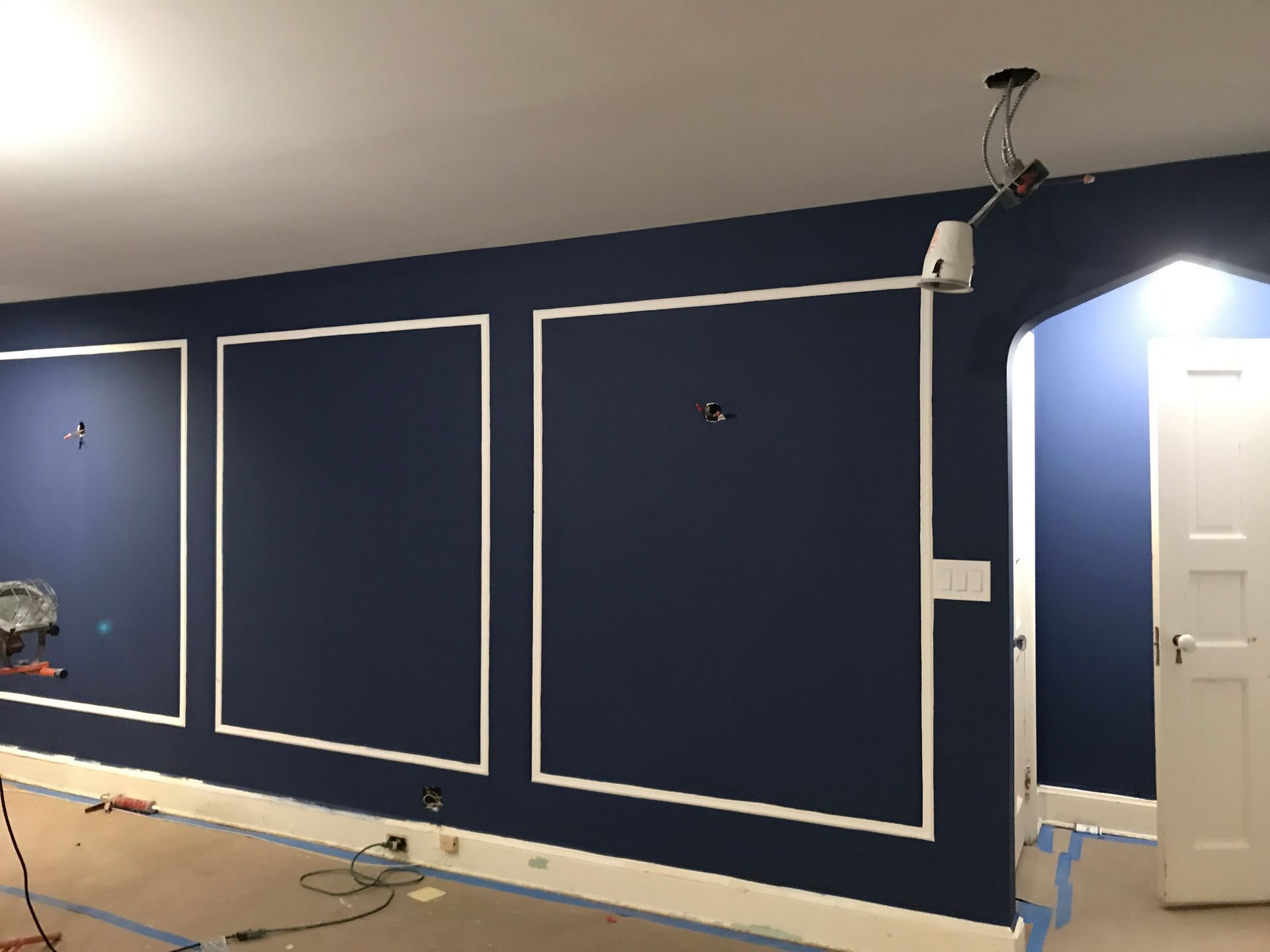 Blue wall with white trim in a room under renovation, with exposed wiring and a doorway on the right