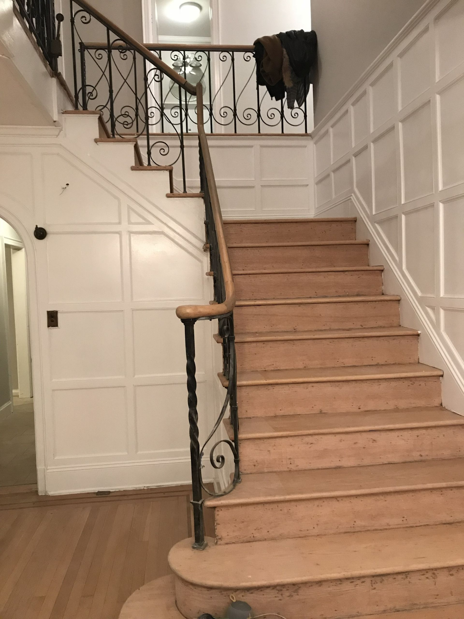 Staircase with beige carpet, white paneled walls, and black wrought-iron railings in a home interior