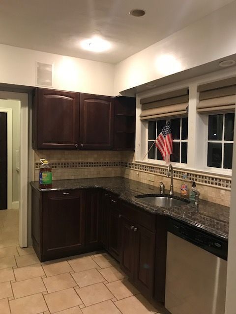 Kitchen with dark wood cabinets, black countertops, stainless dishwasher, and an American flag by the window.