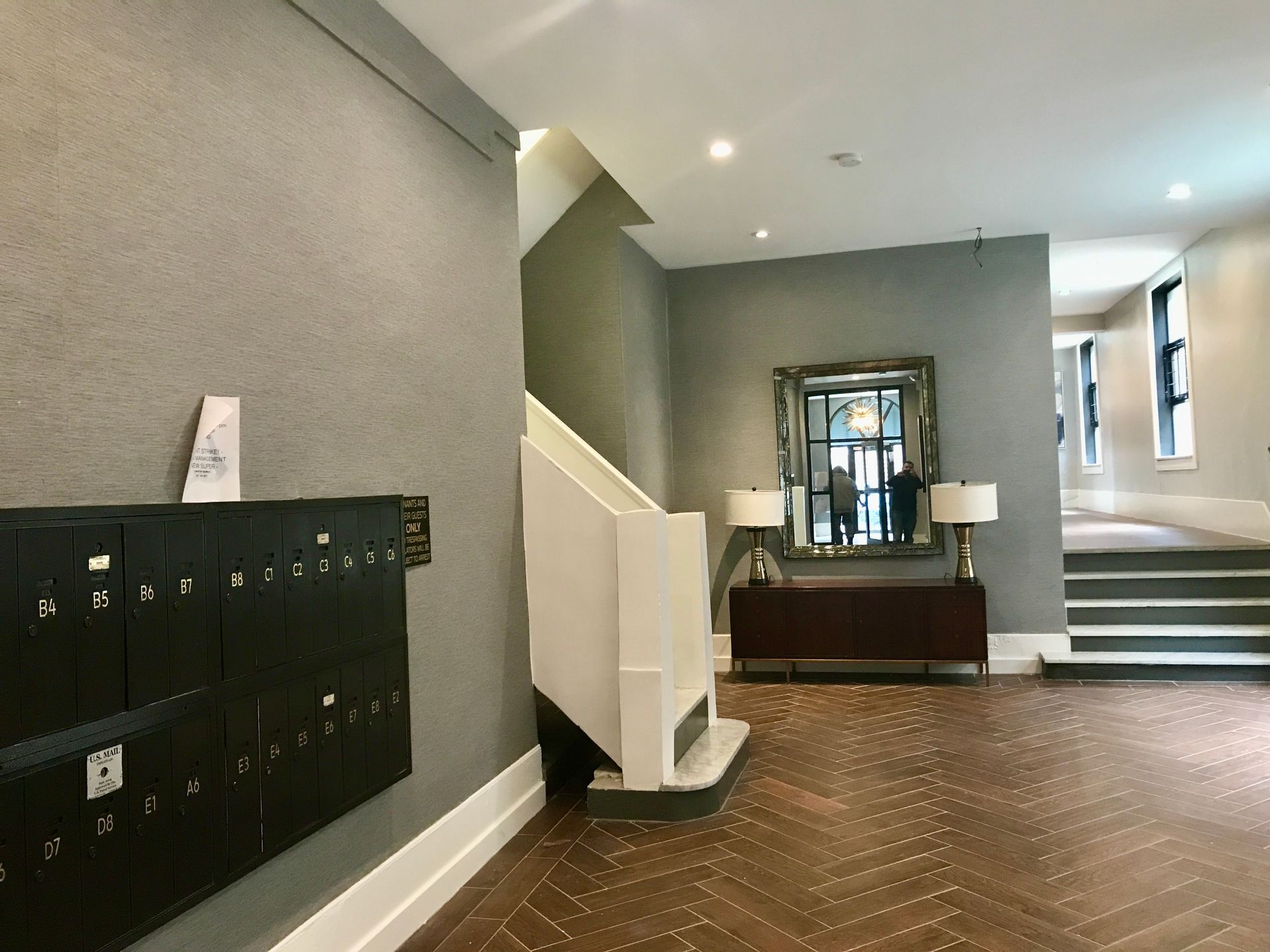 Apartment lobby with mailboxes, staircase, and decorative mirror on a gray wall