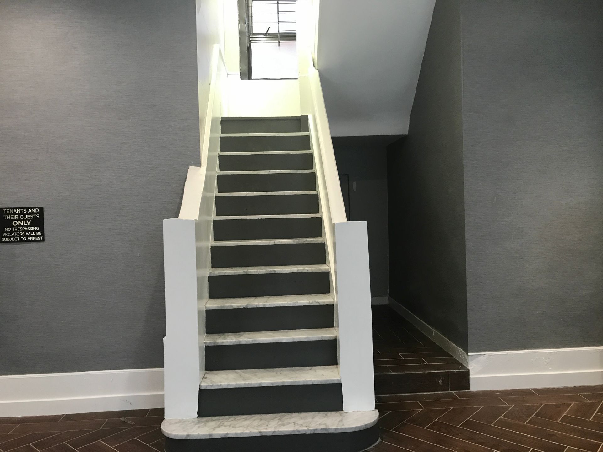 Staircase with dark steps, white railings, and gray walls in an interior hallway.