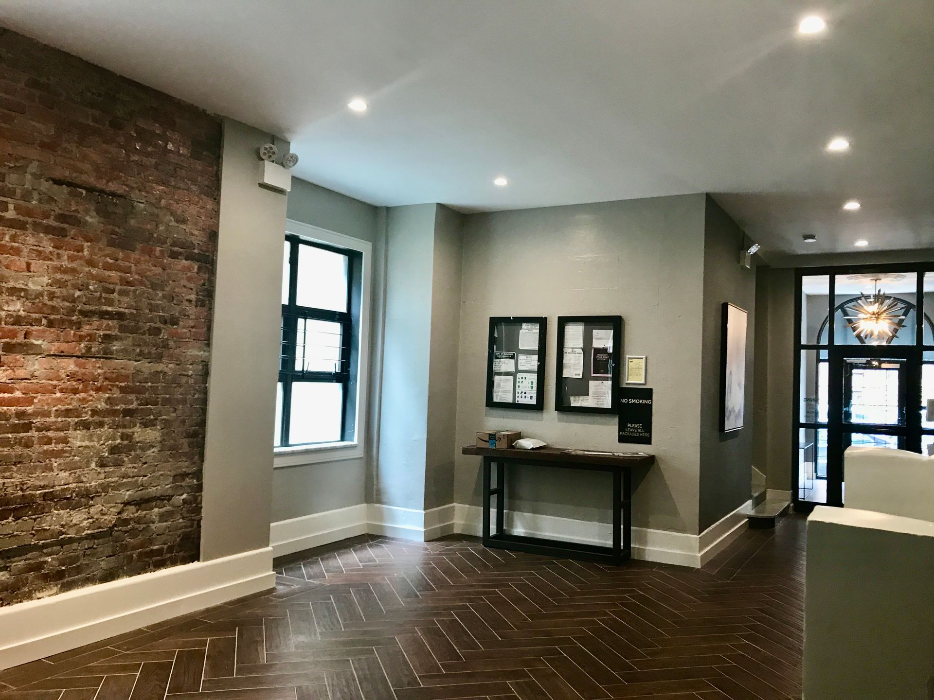 Modern interior hallway with exposed brick wall, windows, herringbone floor, and framed artwork display.