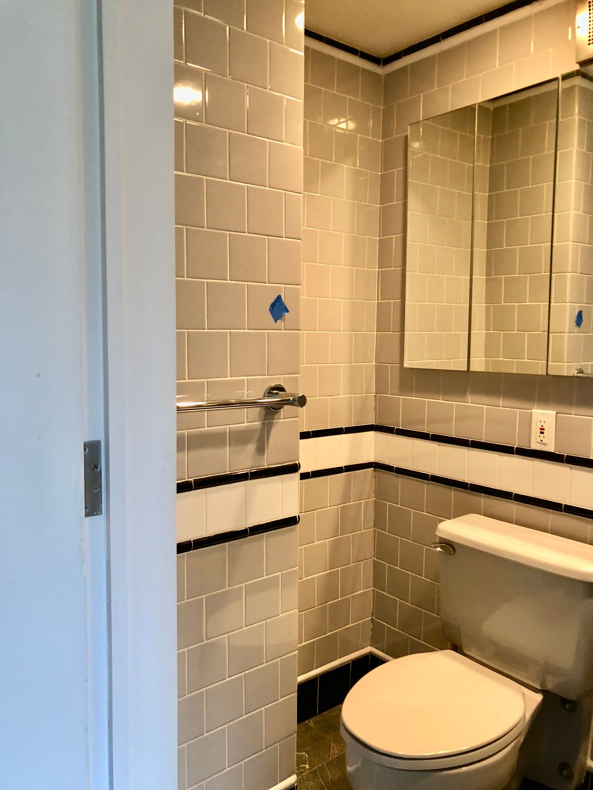 Small tiled bathroom with a toilet and wall-mounted sink in beige and black trim.