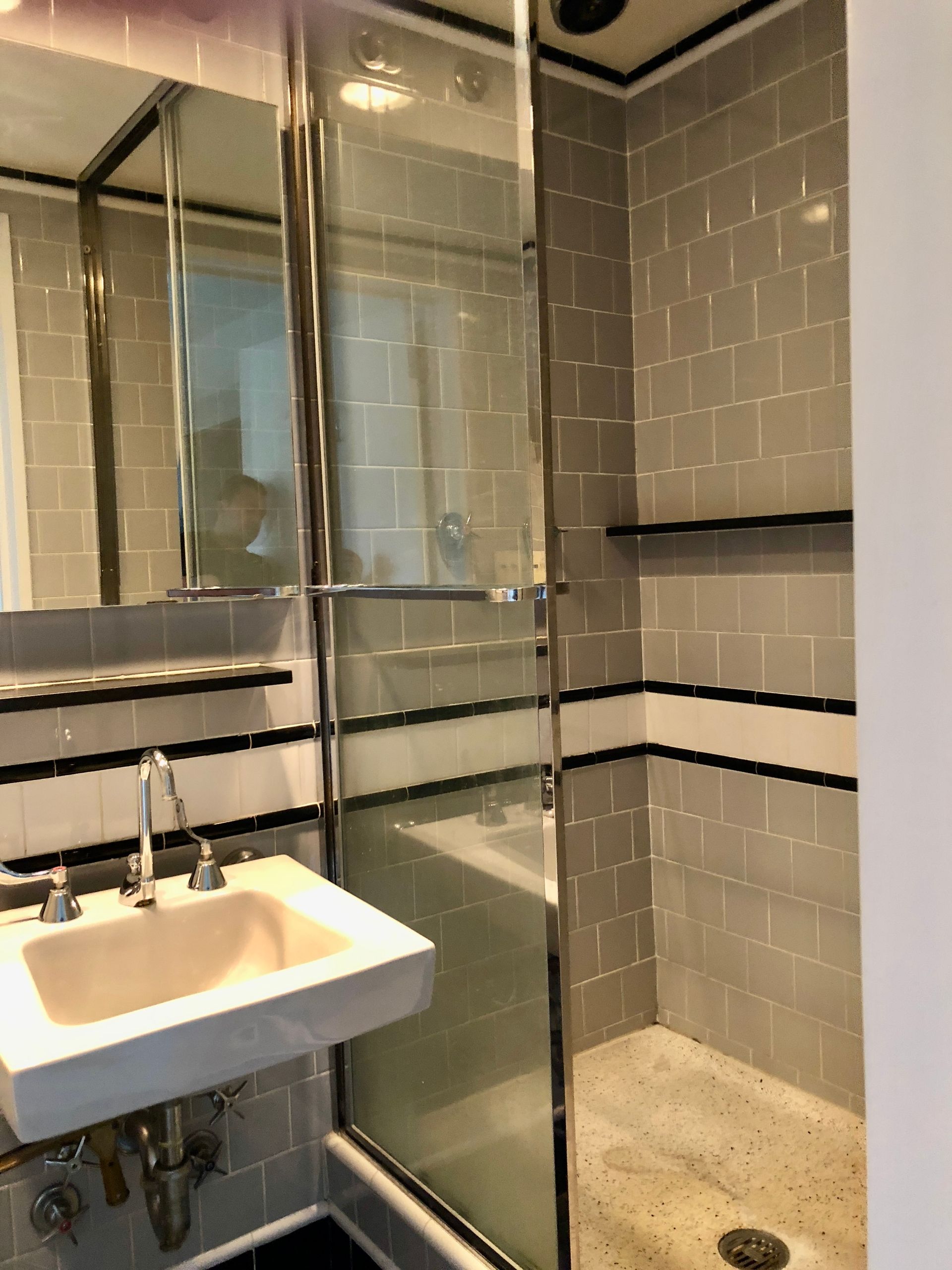 Small bathroom with a white sink, mirrored cabinet, glass shower, and gray tile walls.