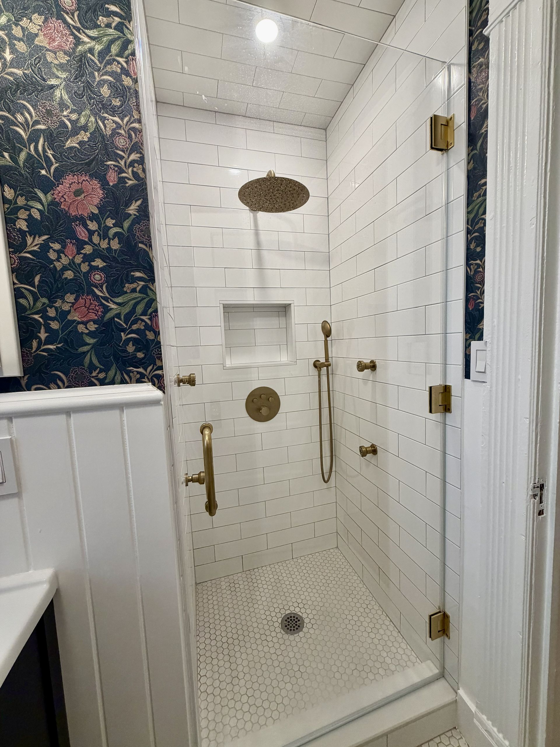 White tiled shower stall with gold fixtures and floral curtains in a bathroom