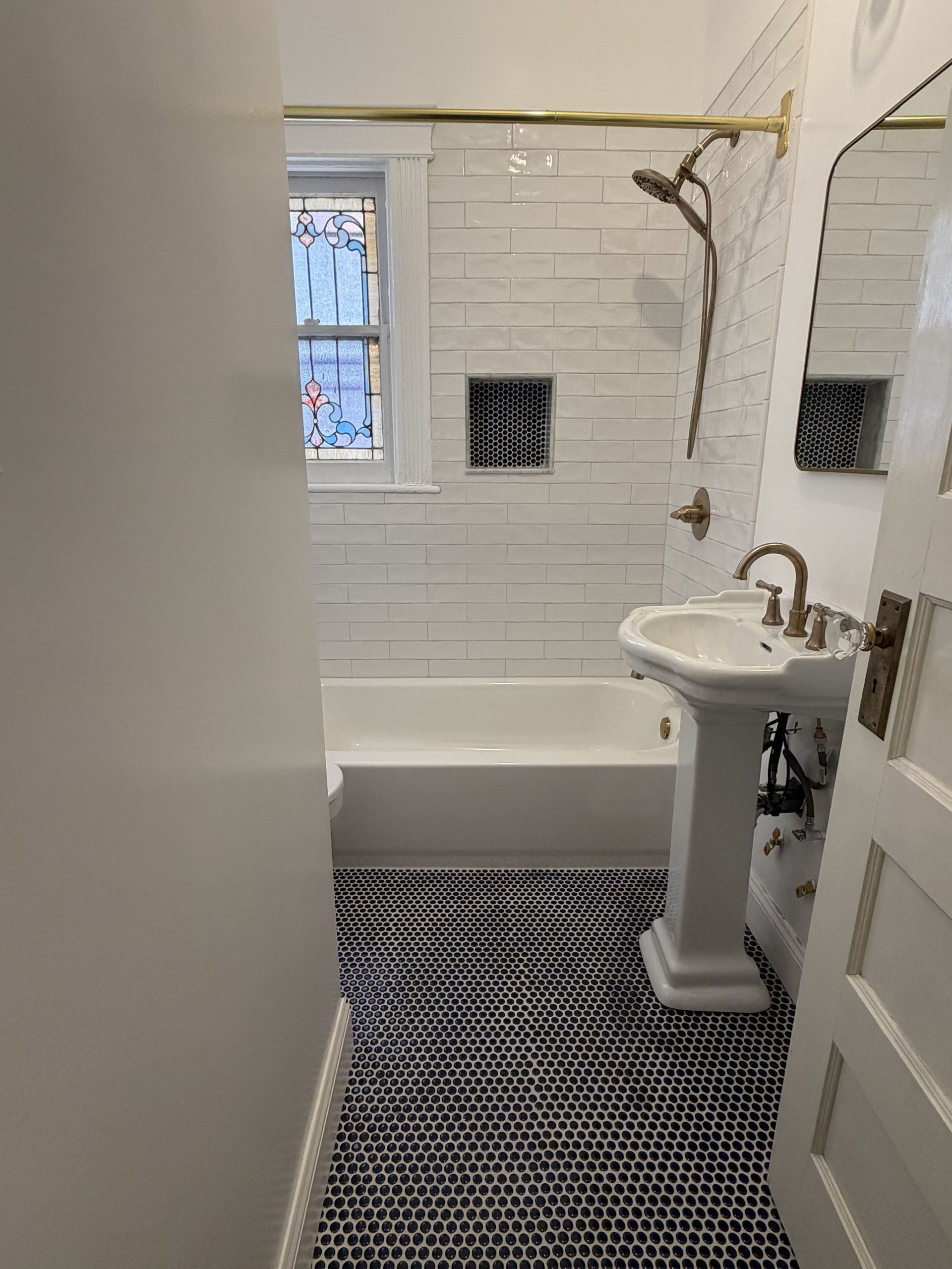 Small bathroom with white subway tile, pedestal sink, bathtub, and black-and-white patterned floor