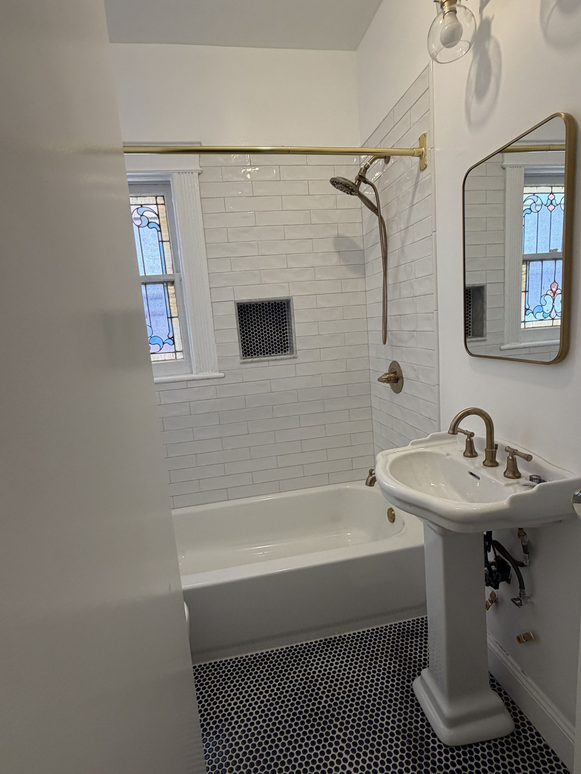 Small bathroom with white tub, pedestal sink, shower curtain rod, and patterned black-and-white floor tile.