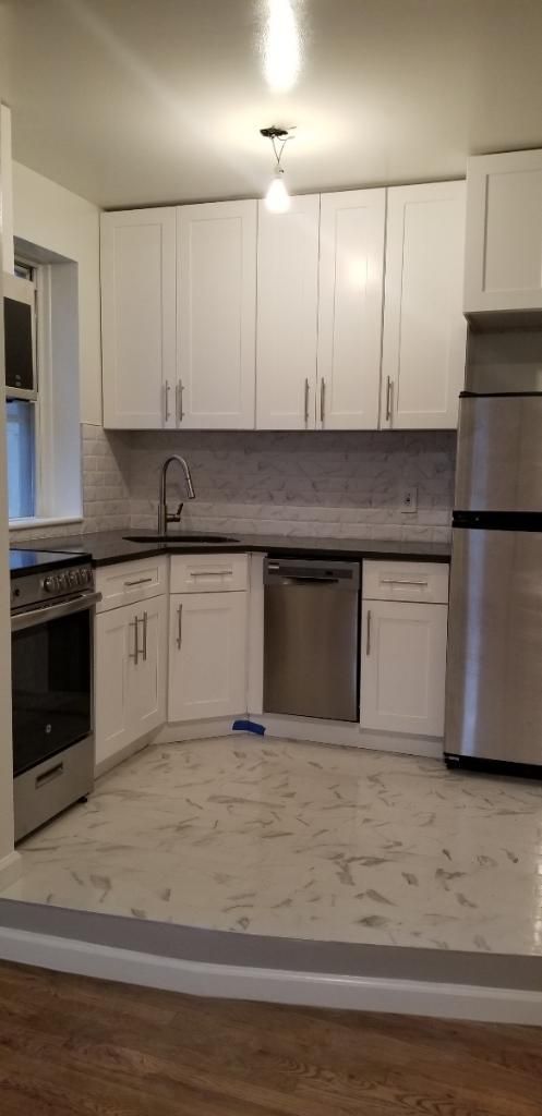 White L-shaped kitchen with cabinets, stainless appliances, gray backsplash, and light tile floor