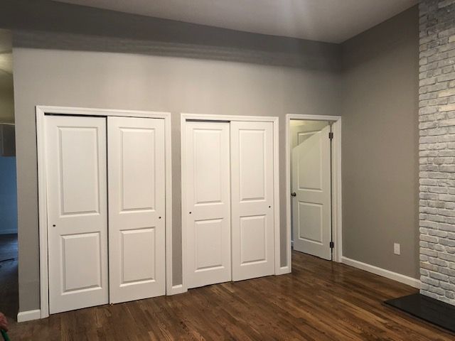 Empty room with brown hardwood floor, gray walls, white closet doors, and a brick fireplace edge.