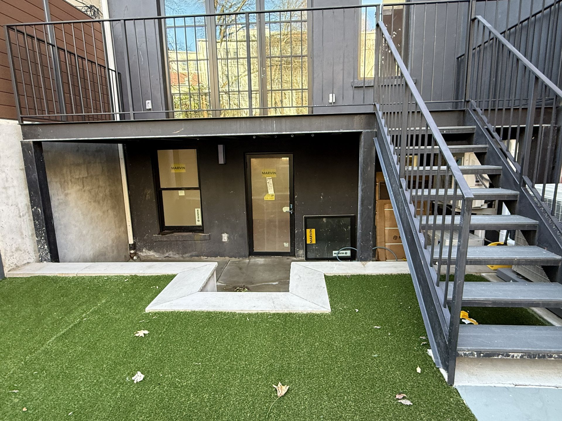 Courtyard view of apartment exterior with stairs, doors, and artificial grass patio