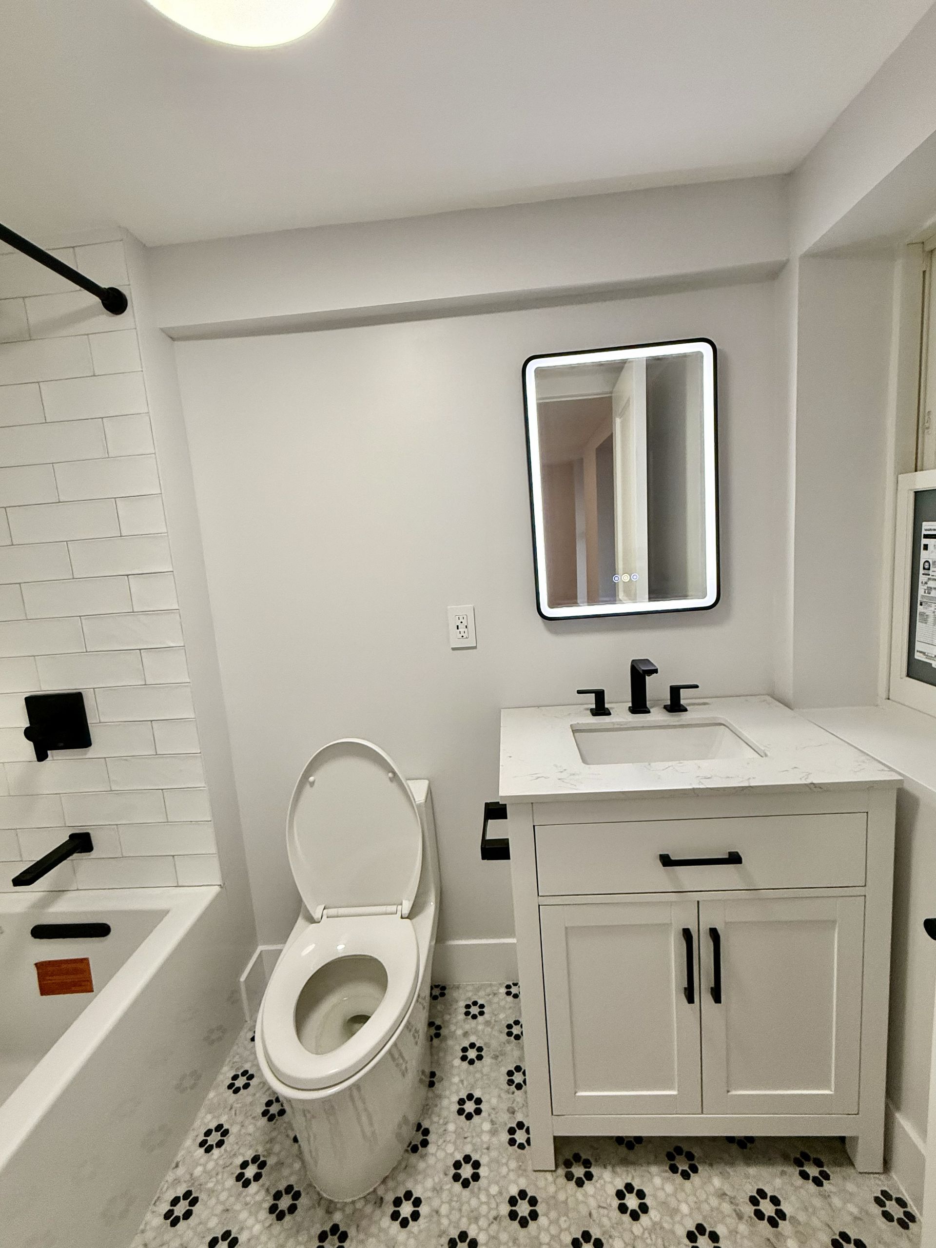 Small bathroom with black-and-white tile, bathtub, toilet, vanity sink, and mirror.