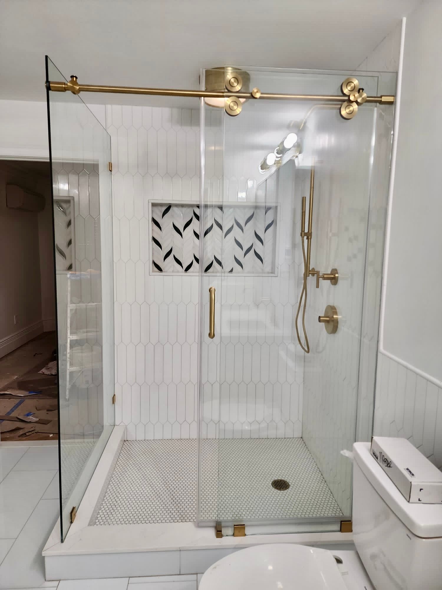 Gold-framed glass shower enclosure in a white-tiled bathroom with a decorative wall niche and bench.