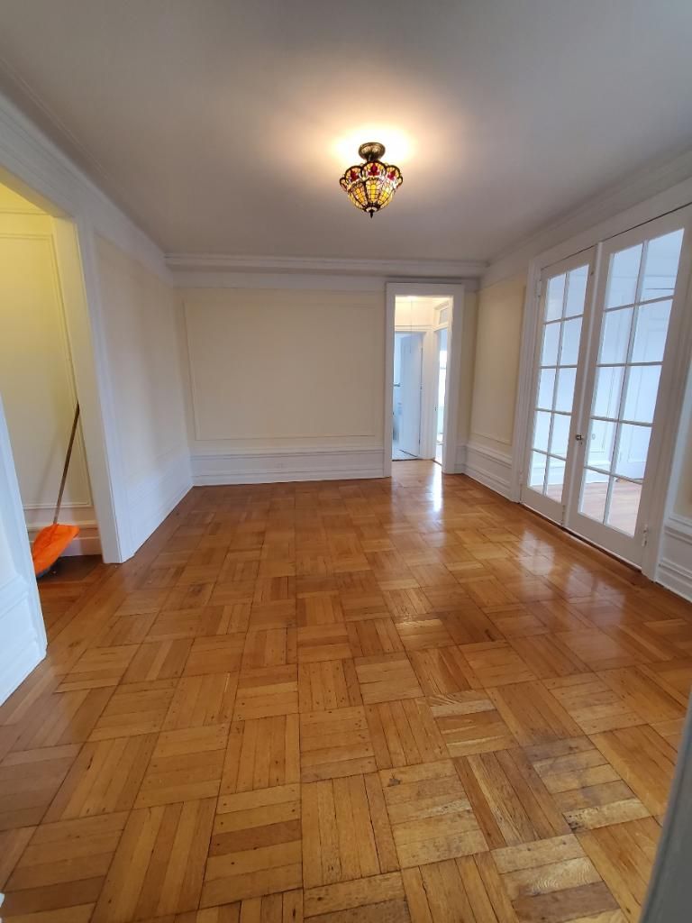 Empty living room with parquet floor, white walls, chandelier, and glass doors to the right.