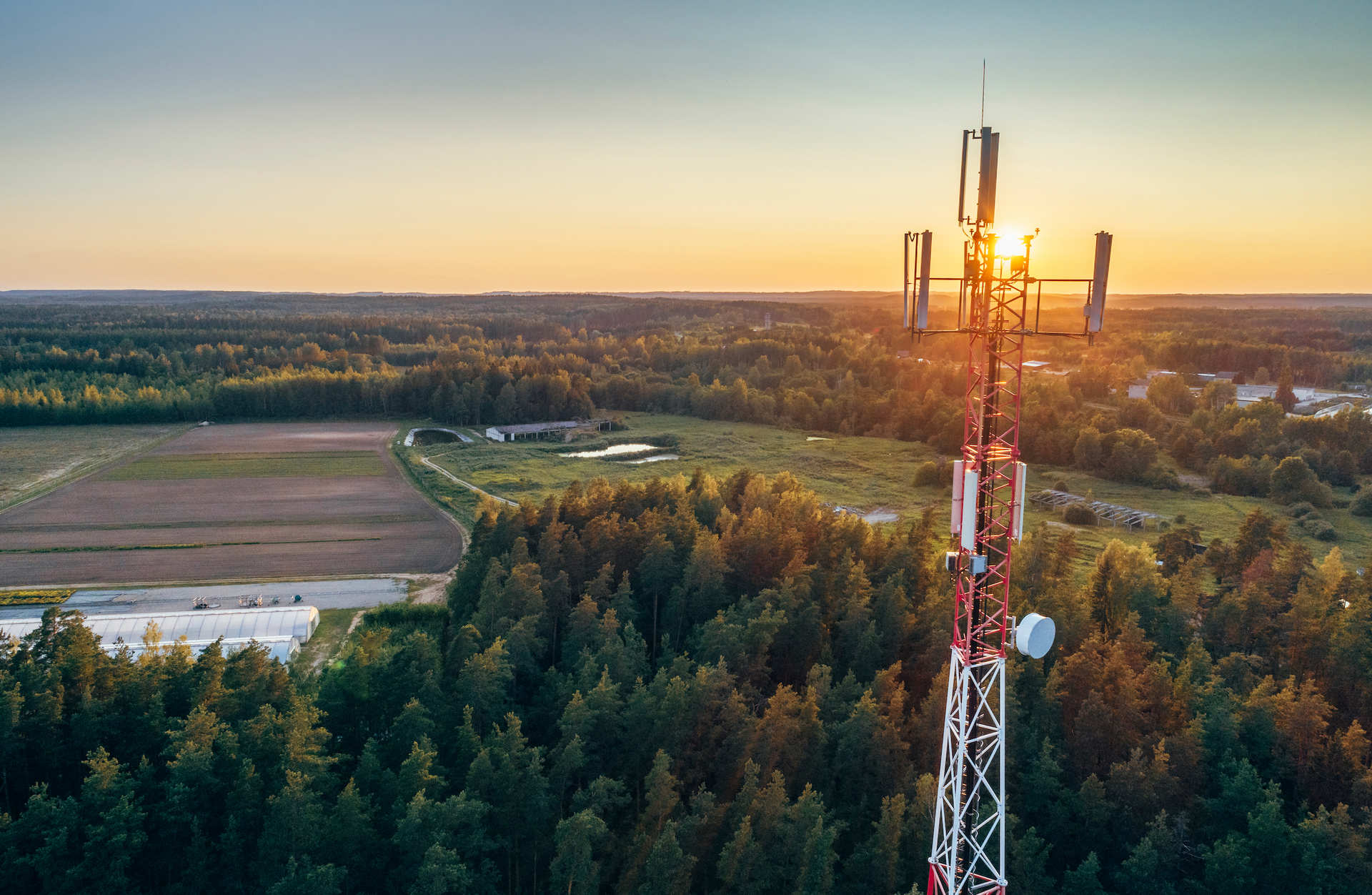 An aerial view of a cell phone tower in the middle of a forest at sunset.