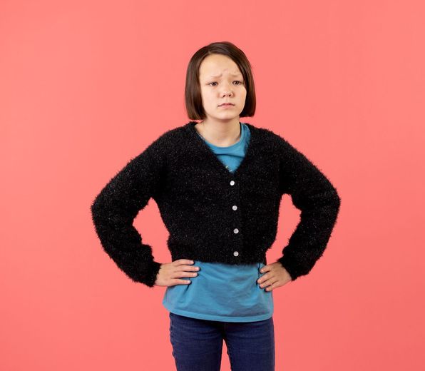 A young girl wearing a black cardigan and a blue shirt is standing with her hands on her hips.