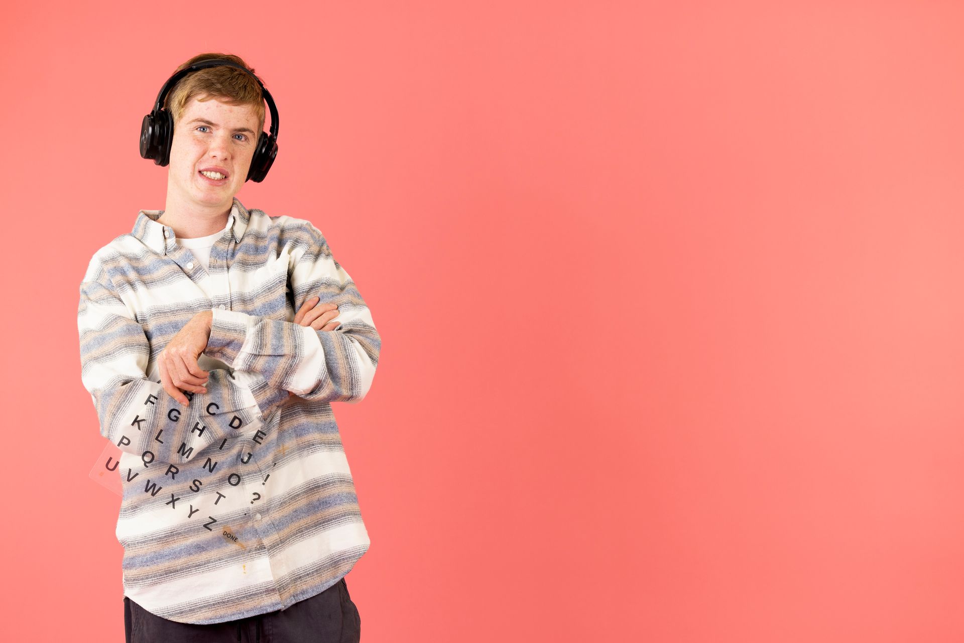 A young man wearing headphones and a sweater is standing with his arms crossed.