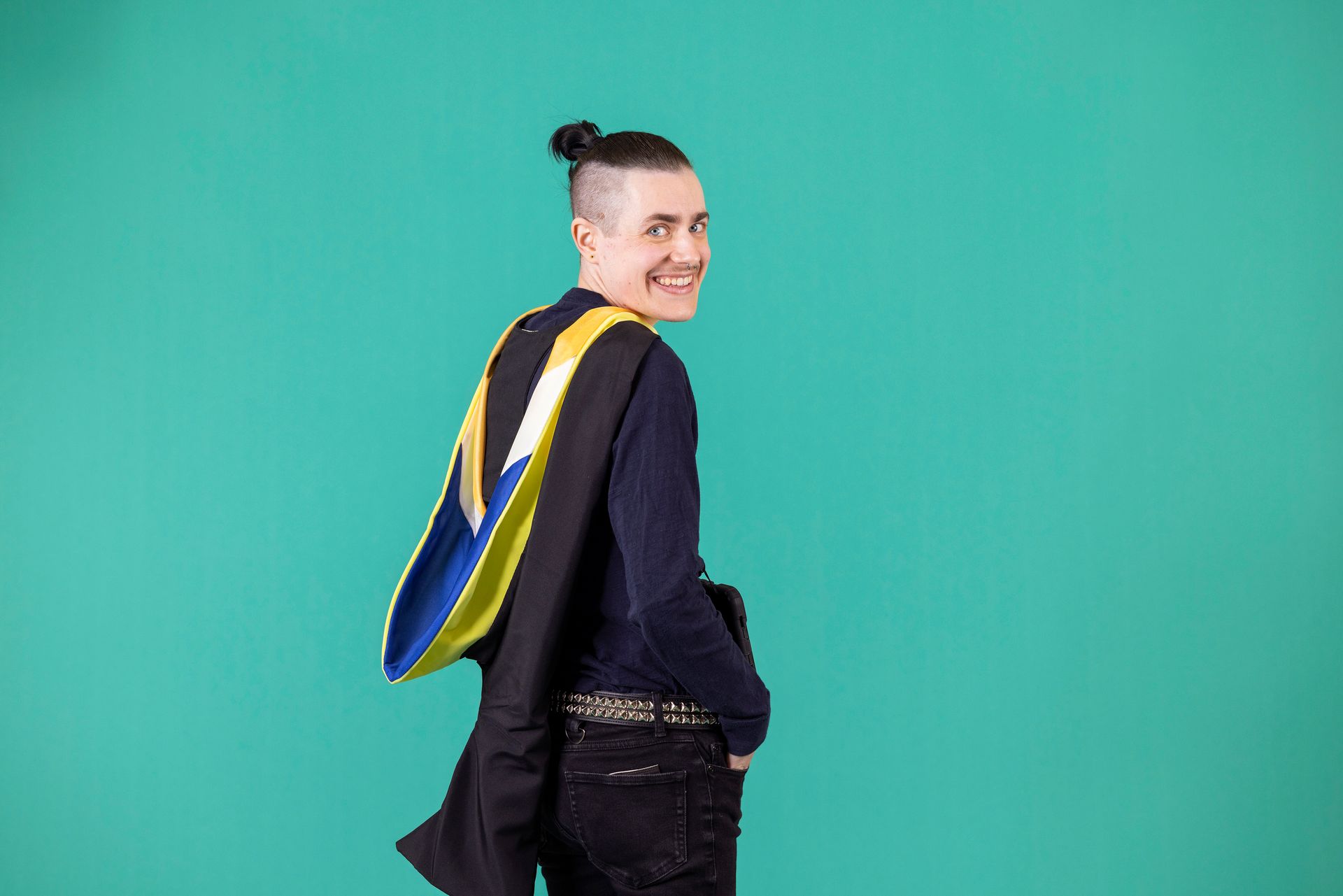 A man wearing a graduation cape is standing in front of a blue background.