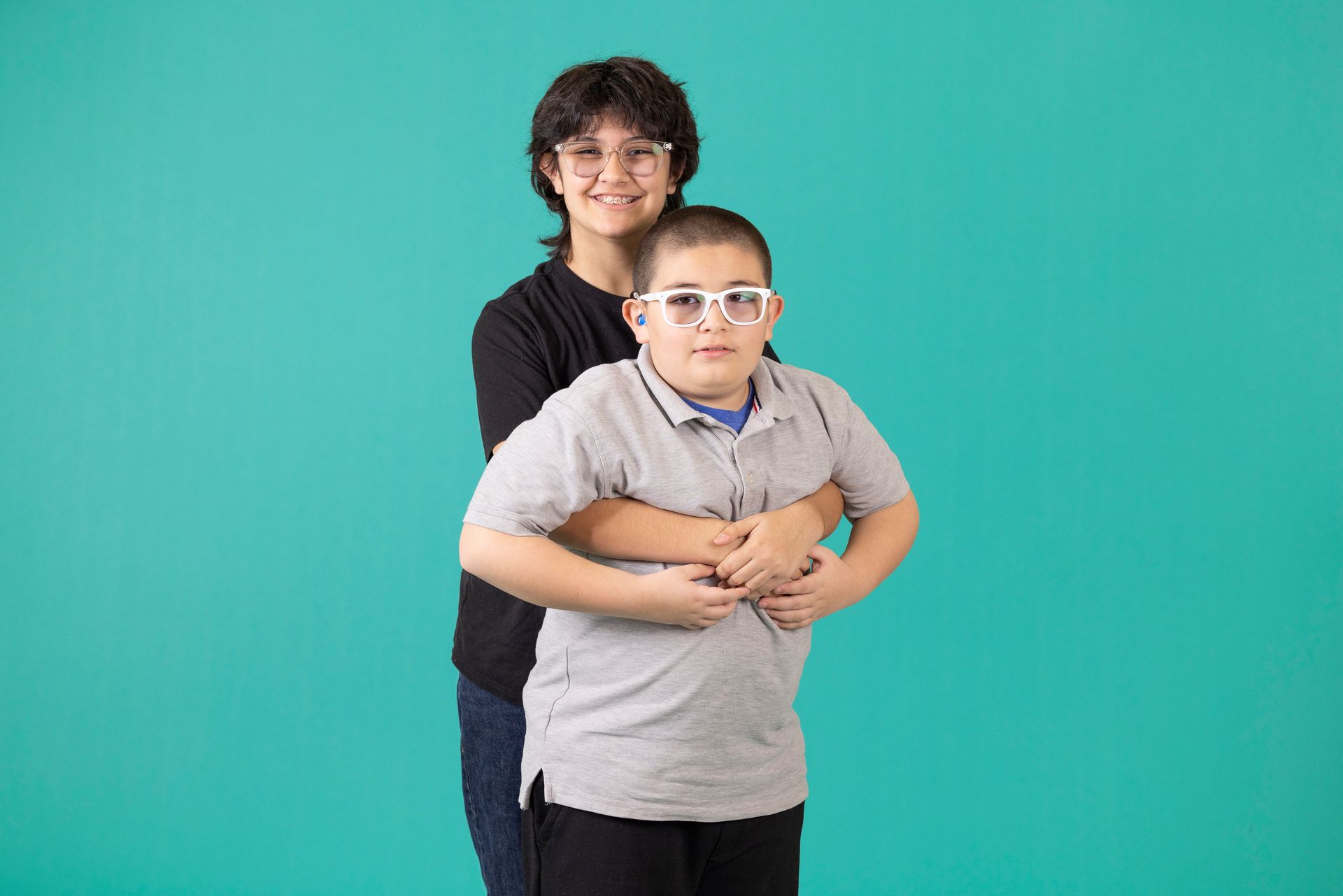 A woman is hugging a boy with glasses on a blue background.