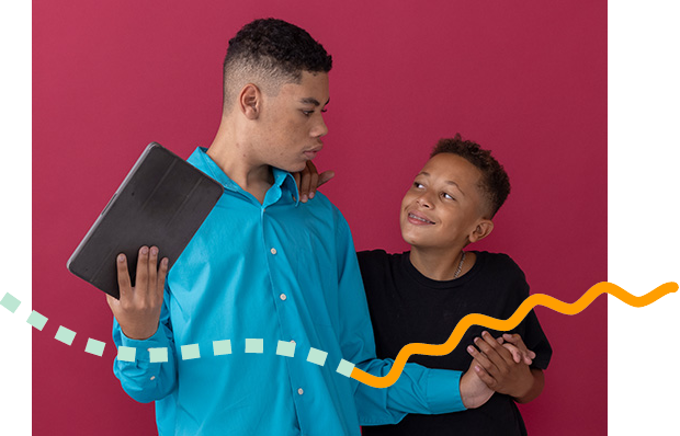 2 brothers standing next to each other . 1 boy is holding a tablet.