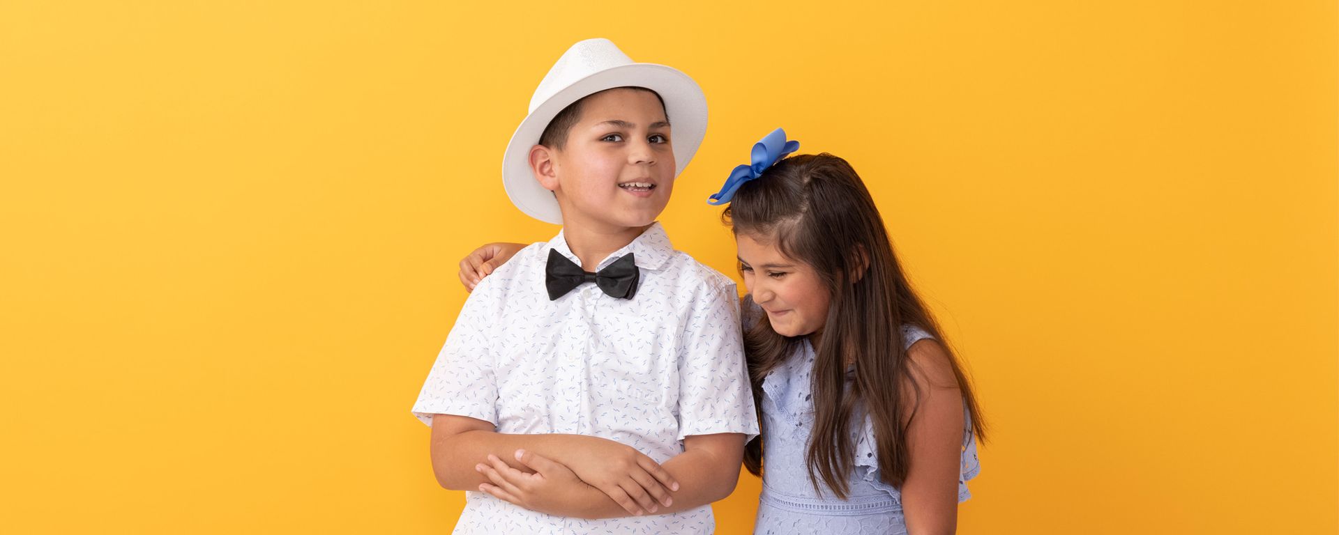 A boy and a girl are standing next to each other on a yellow background.