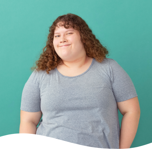A woman with curly hair is wearing a grey shirt and smiling