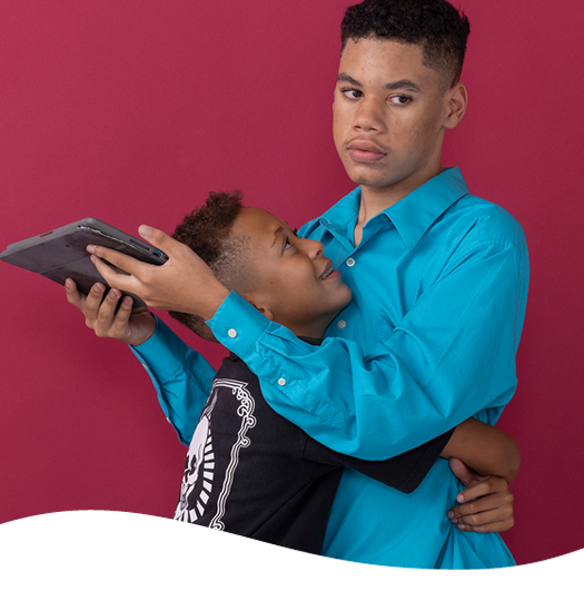 A man in a blue shirt is hugging another man who is holding a tablet
