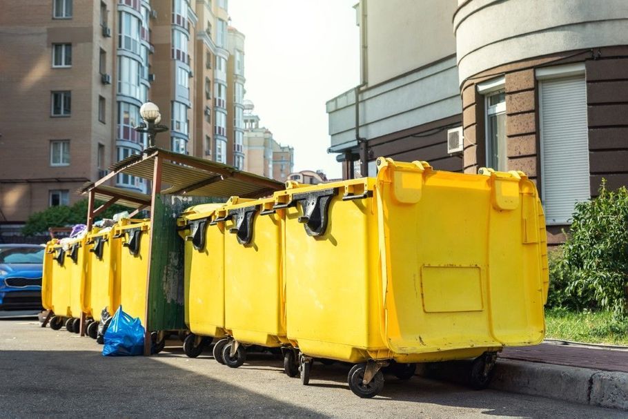 Yellow dumpsters lined up on a city street beside apartment buildings
