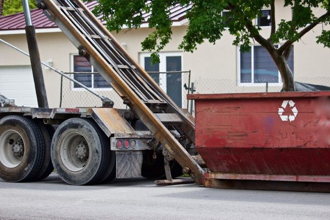Dumpster being loaded onto a truck with metal rails in a residential driveway.