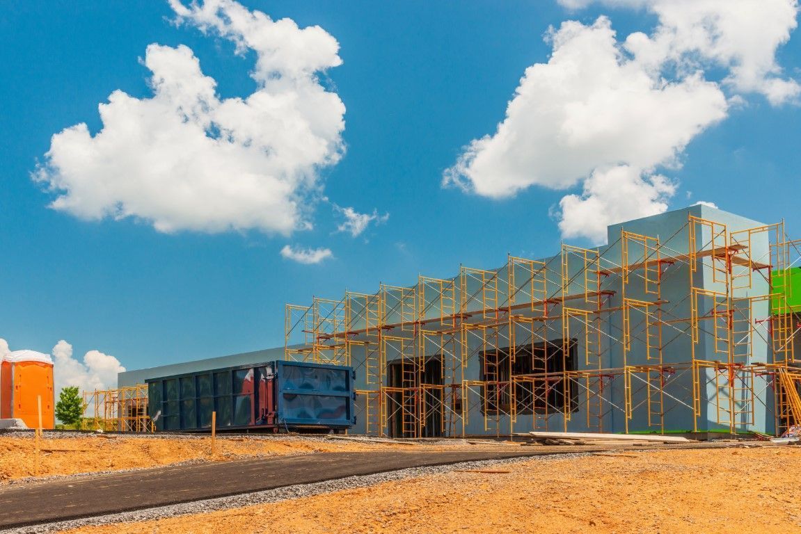 Construction site with steel framework, blue truck, and scaffolding under a bright sky with clouds